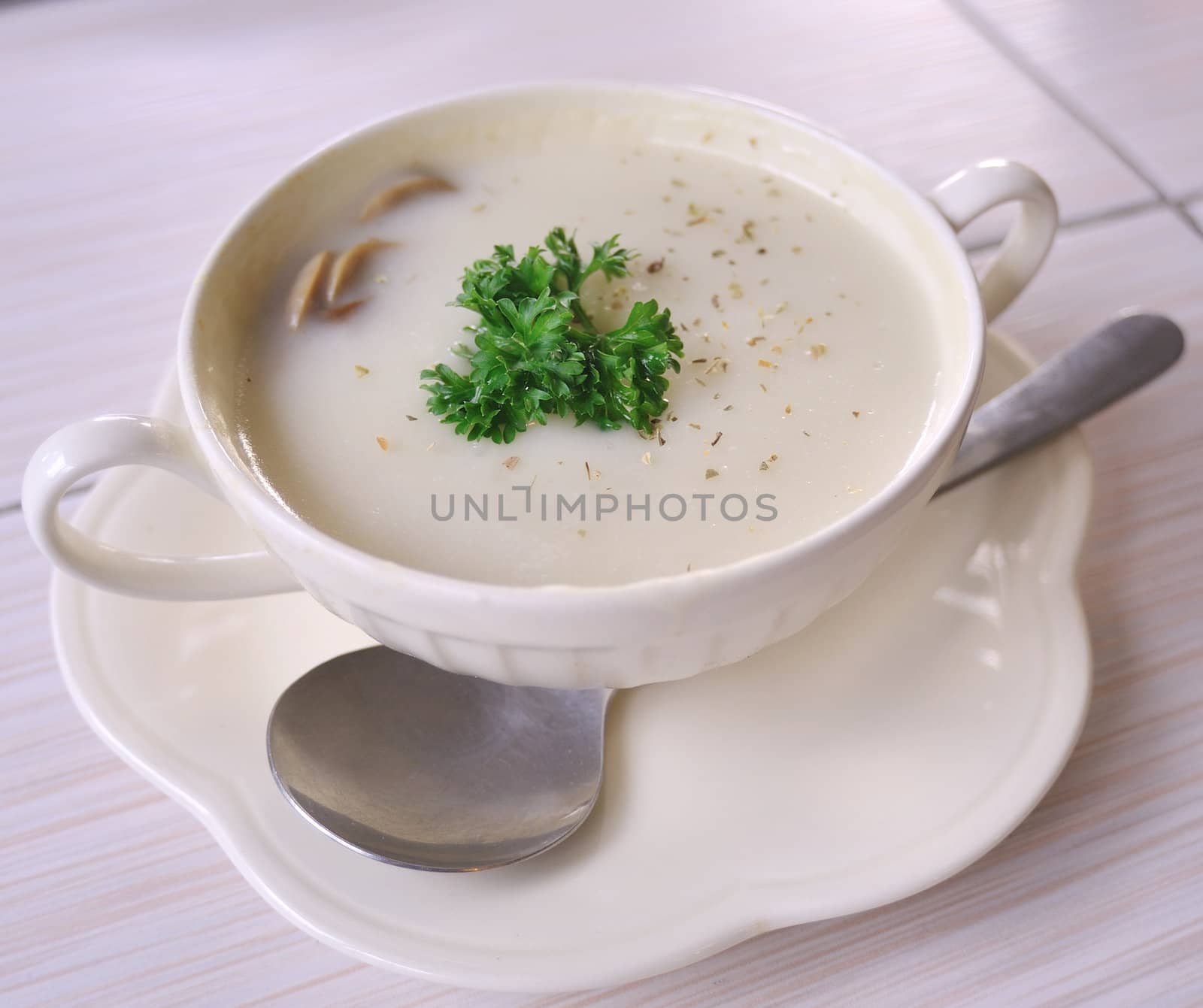 Mushroom soup with parsley in white ceramic bowl and spoon by sommai
