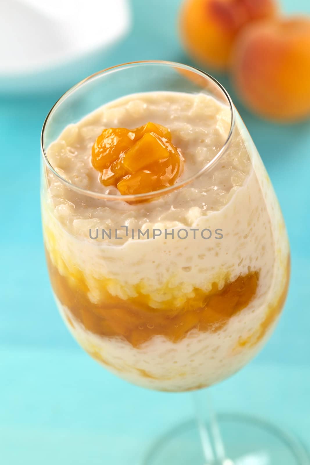 Fresh homemade rice pudding with peach compote served in a high glass (Selective Focus, Focus on the front of the peach compote on top of the dessert)