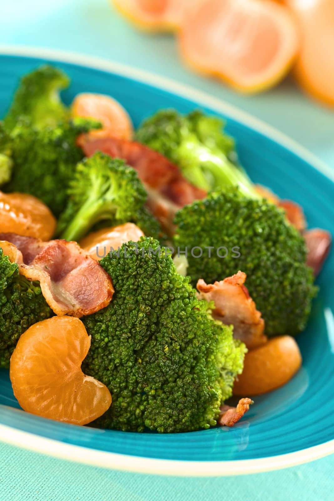 Fresh homemade broccoli, mandarin and bacon salad on blue plate (Selective Focus, Focus on the broccoli and the mandarin in the front)