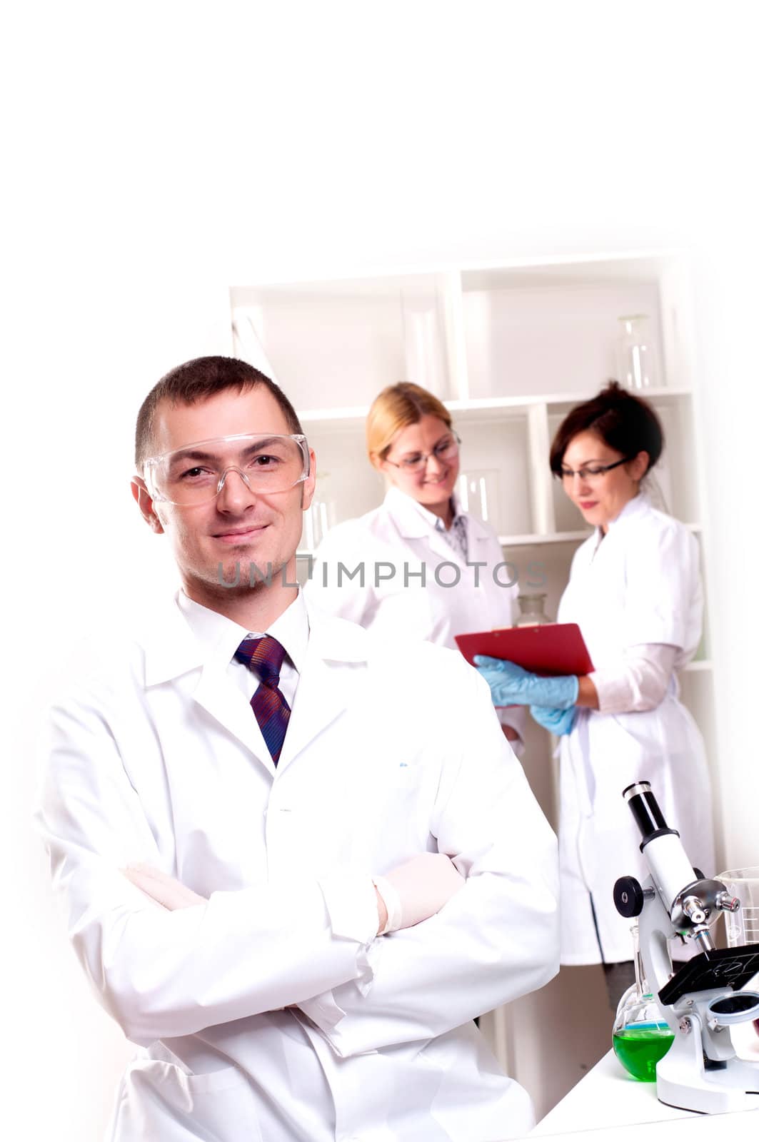 Three doctors are smiling at the camera in a doctors' office. Horizontally framed shot.