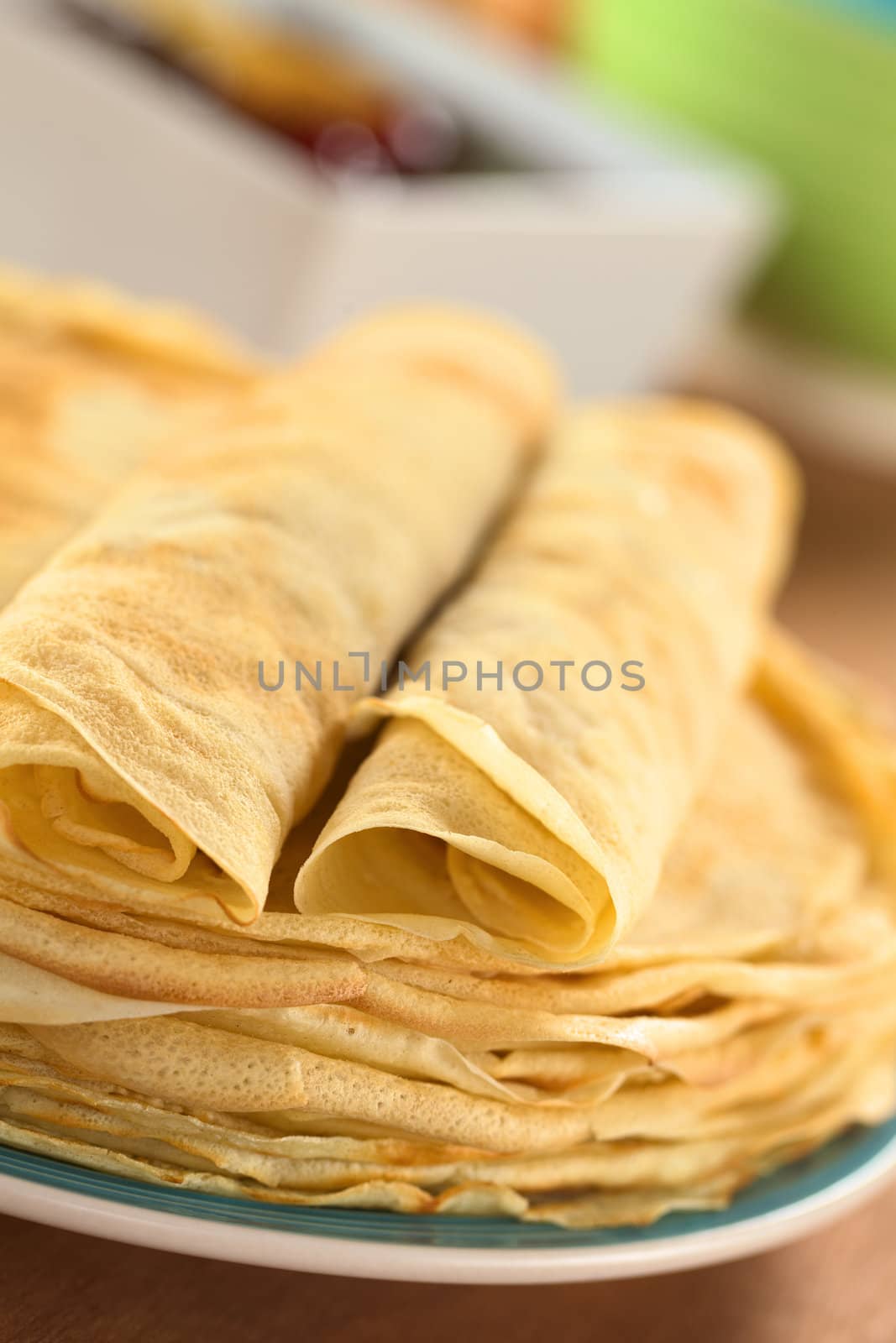 Fresh homemade crepes piled on plate with two rolled crepes on top (Selective Focus, Focus on the front of the right rolled crepe)