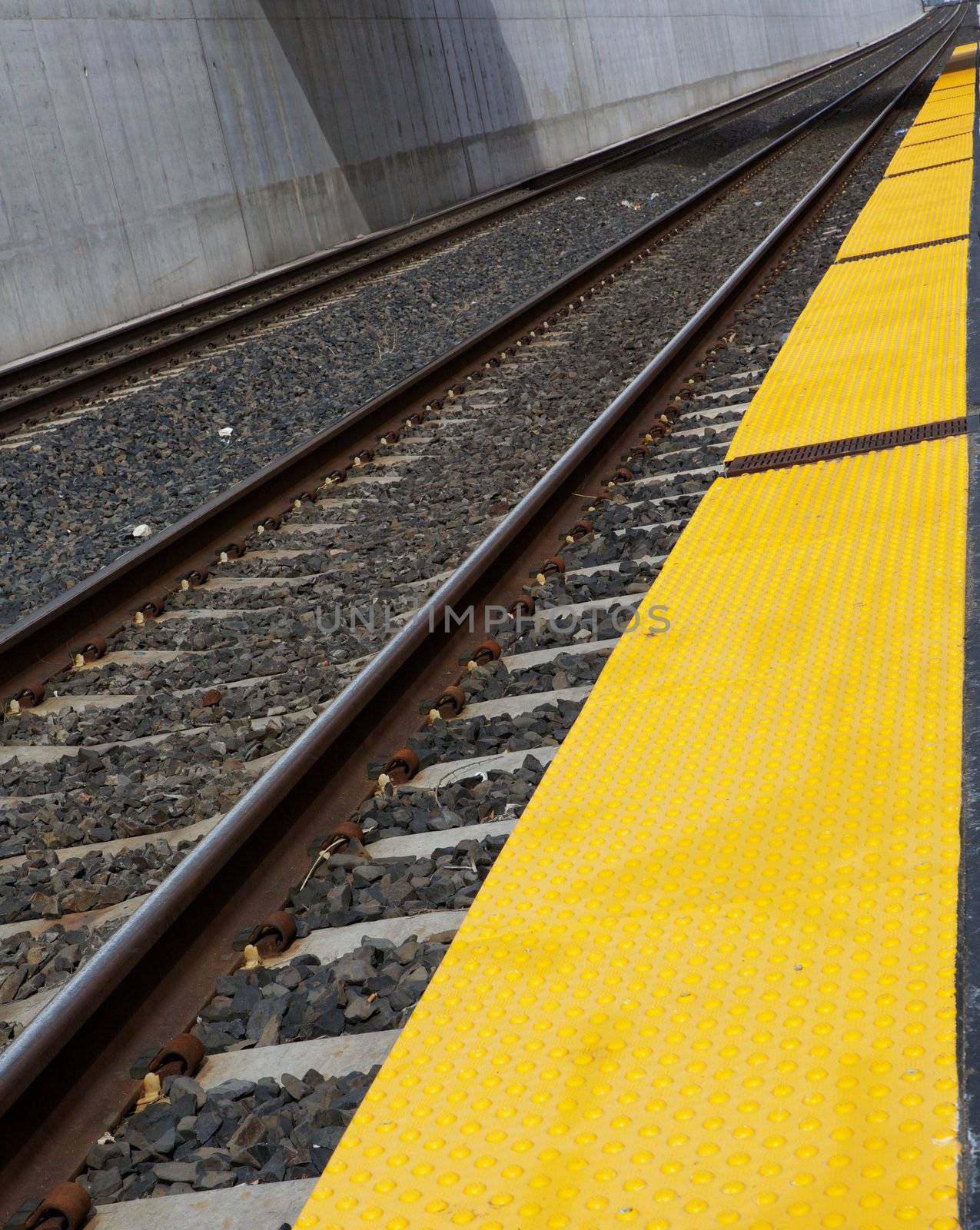 Diminishing straight train tracks at station with yellow boarding area