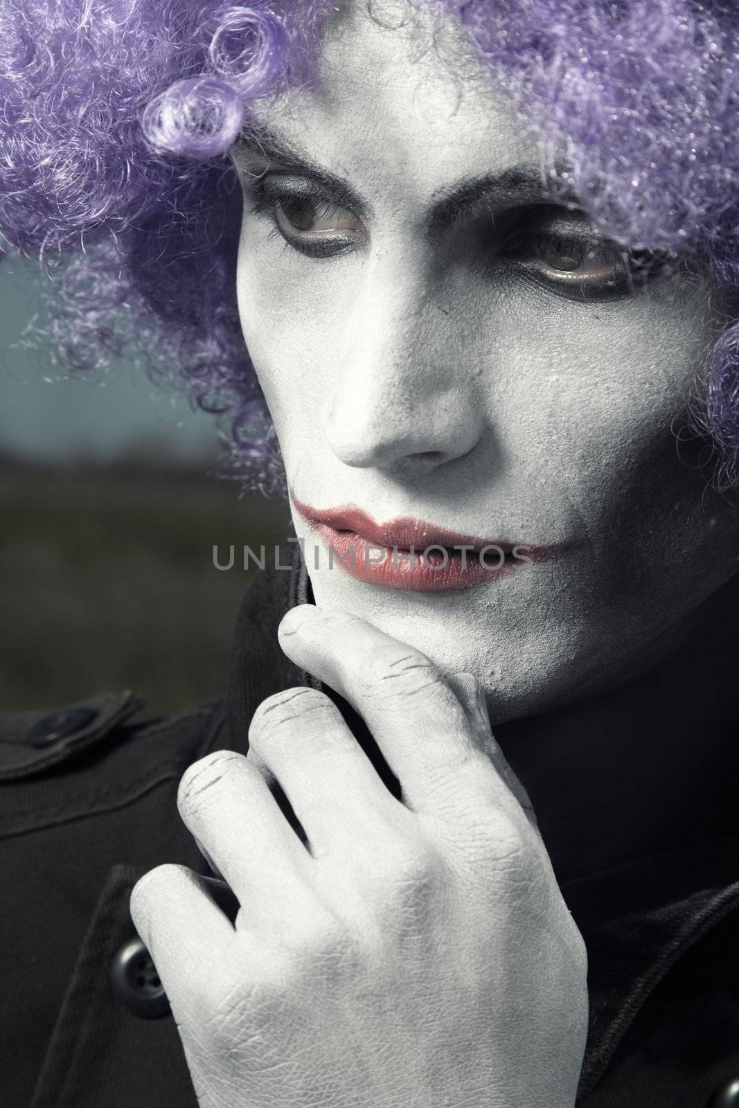Single sad clown with theatrical makeup and wig. Vertical photo with dramatic colors and toning