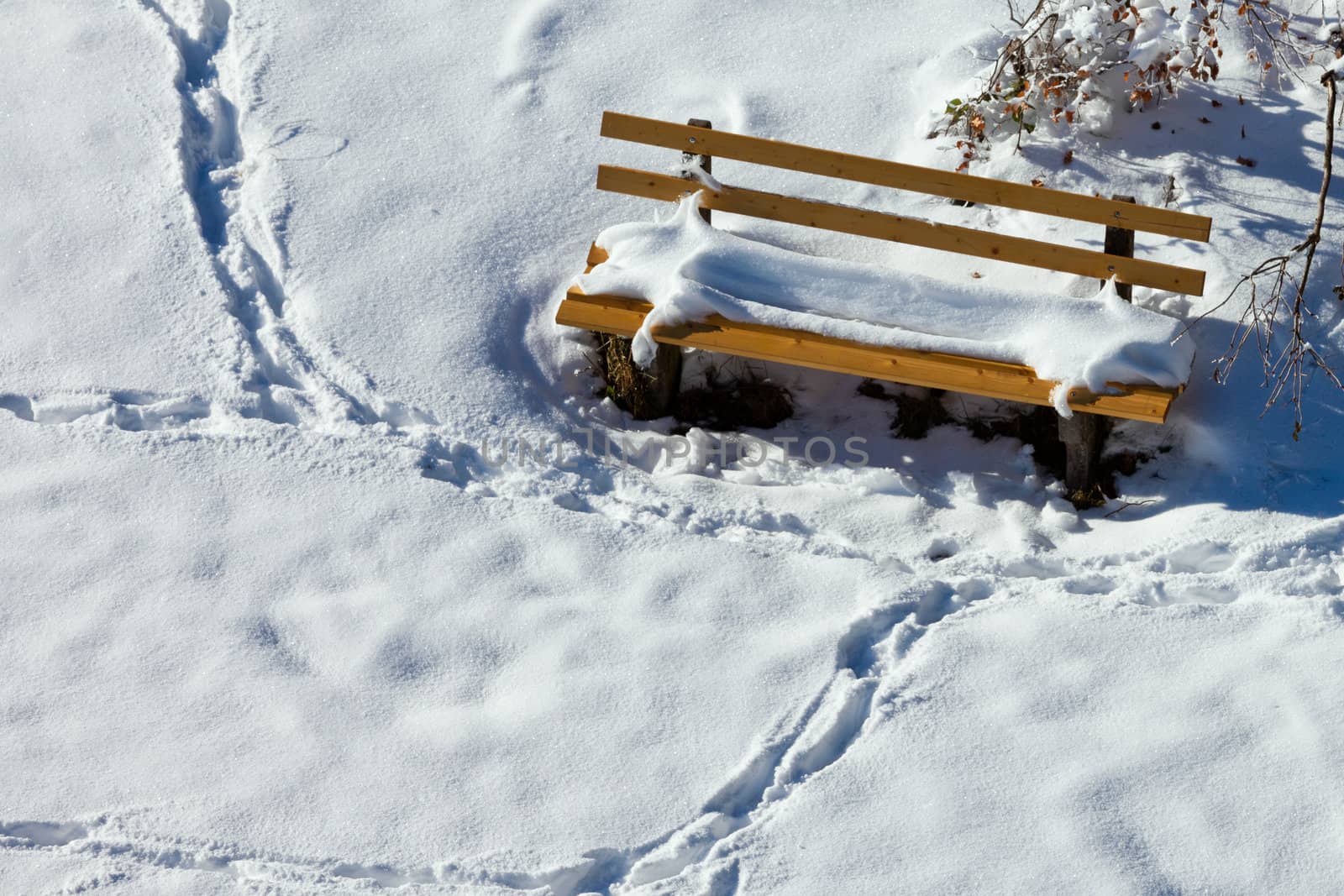 Top view of snow covered wooden park bench with human foot print tracks in freshly fallen snow around it.