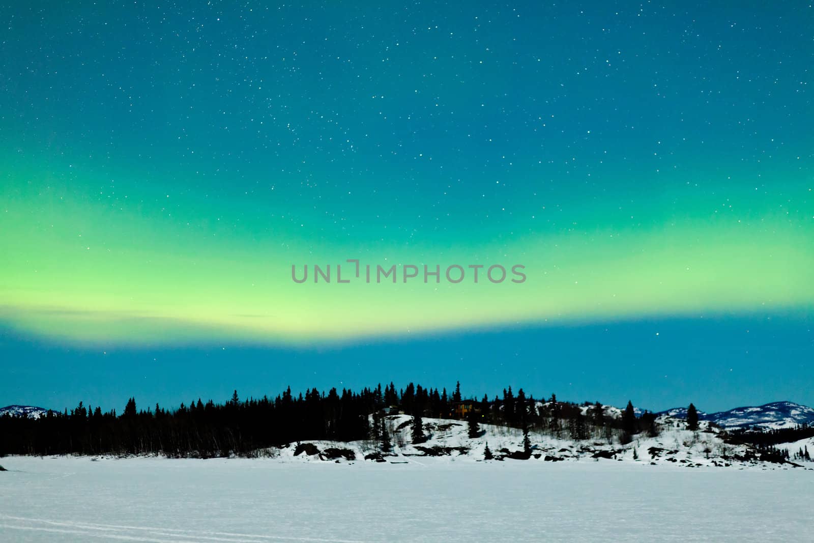 Spectacular display of intense green Northern Lights or Aurora borealis or polar lights over snowy northern winter landscape