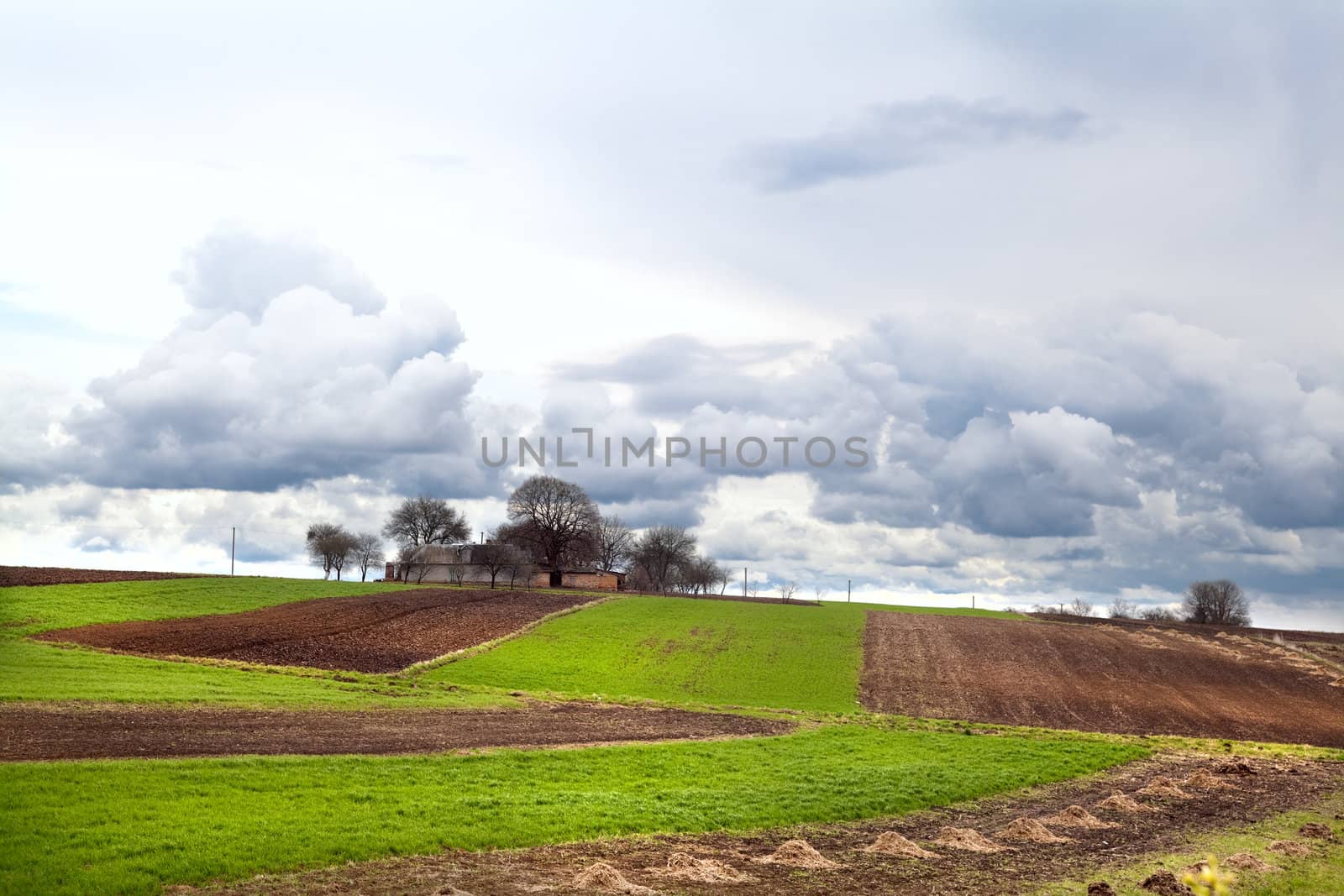 view on village among plowed fields and pastures over clouded sky