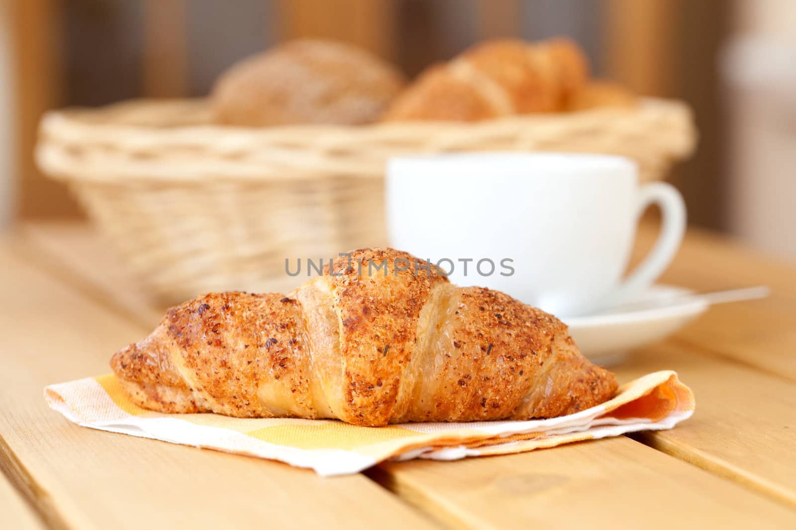 Fresh croissant and white cup coffee, on a wooden table