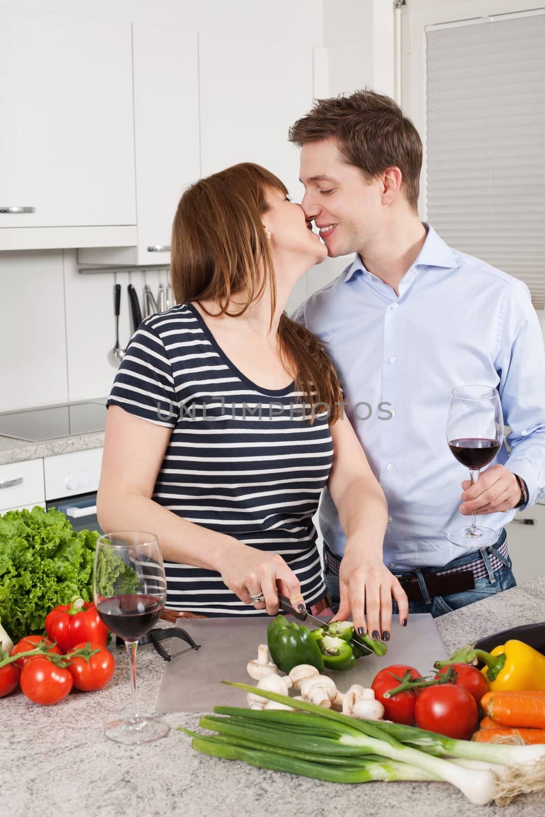 Photo of a young couple preparing salad in their kitchen and drinking wine.