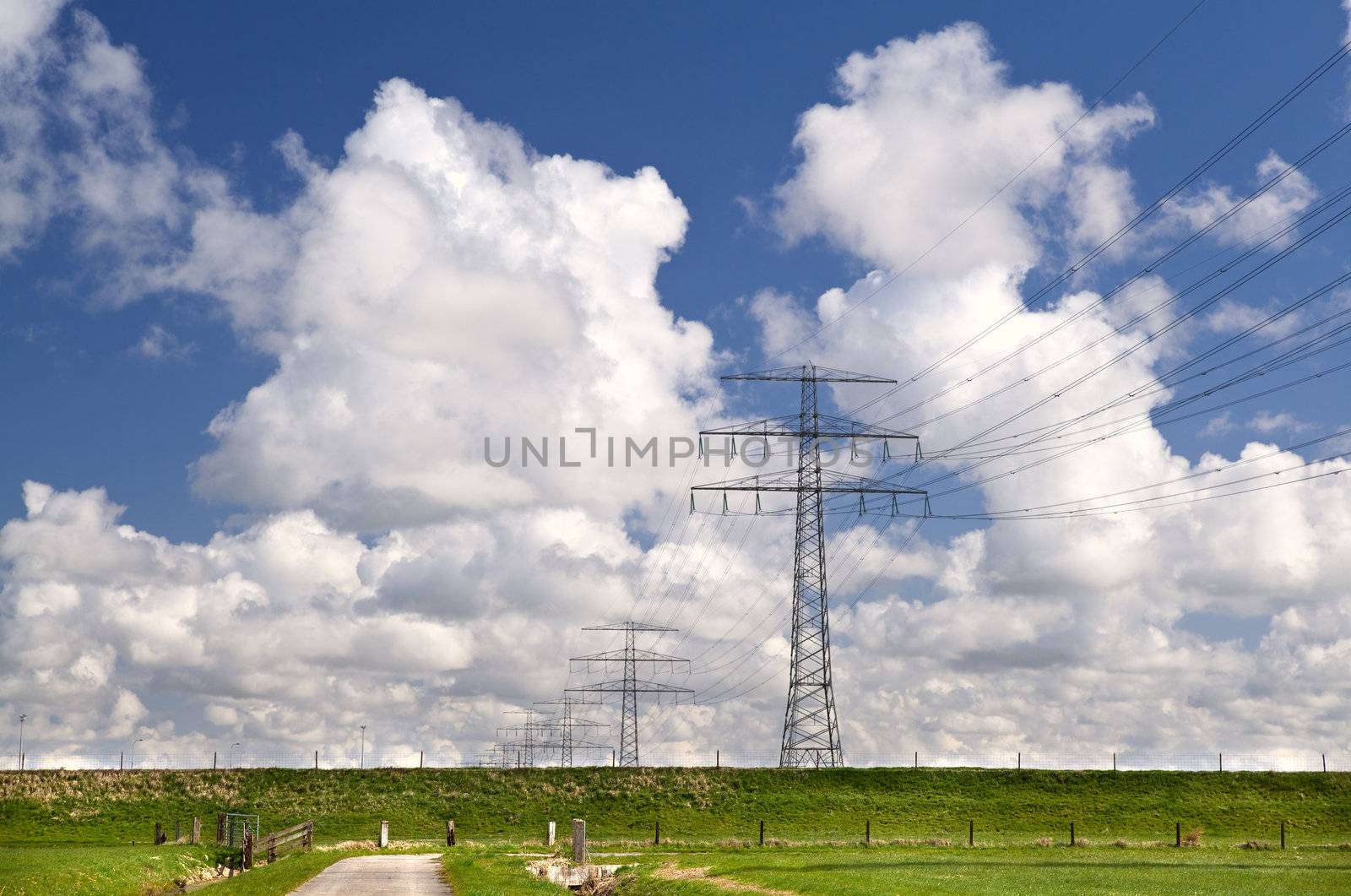 plain Dutch landscape with high-voltage line and beautiful blue sky with puffy white clouds