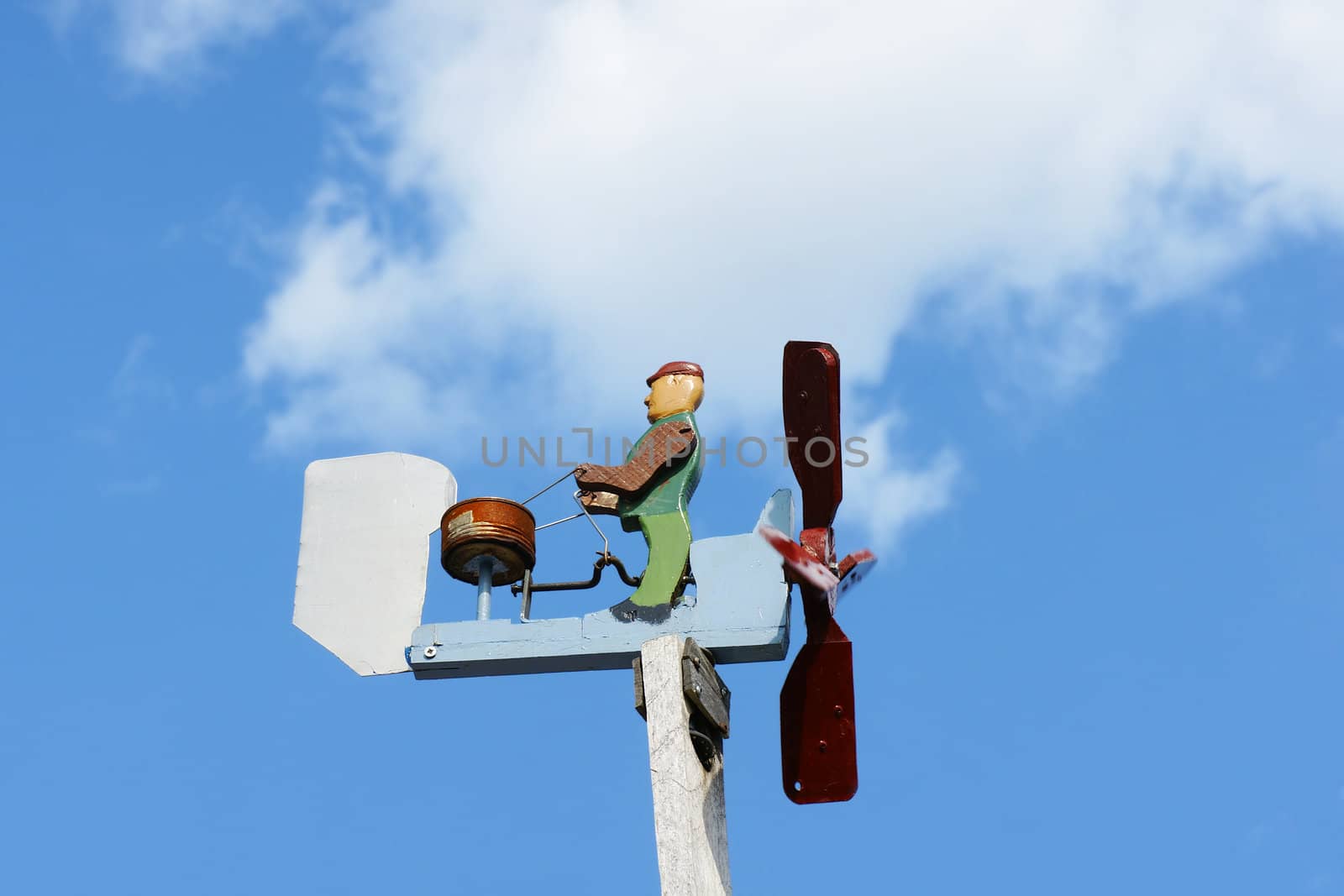 Hand crafted little wooden drummer weathervane, plays music when it is windy, over brigh blue sky.