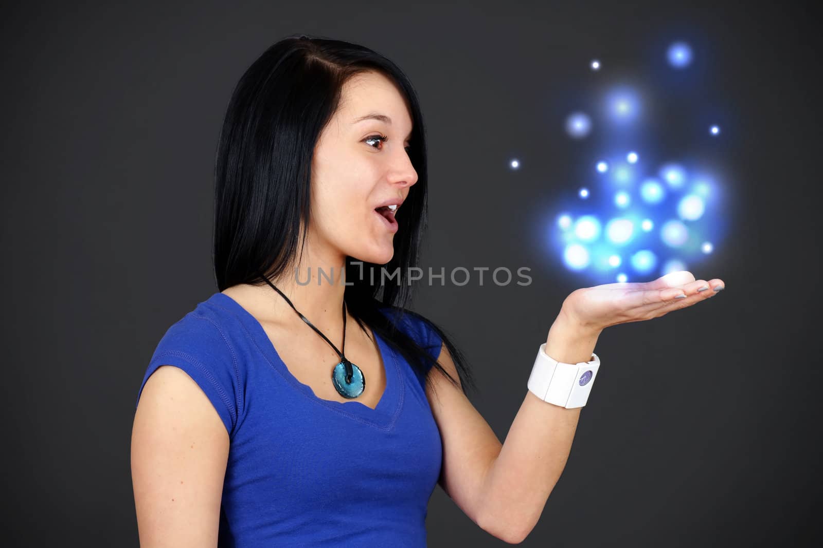 Profile portrait of an amazed young woman or student holding something up in her hand filled with magical lights, fun advertisement.