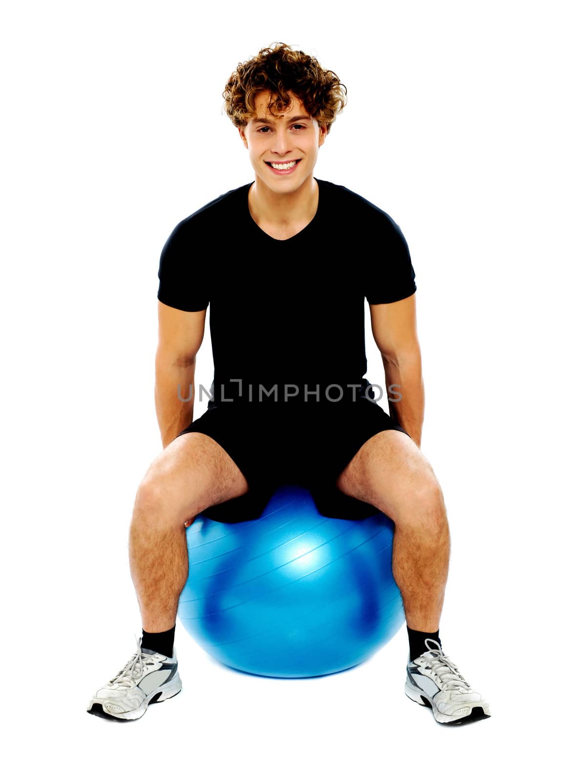 Handsome guy seated on exercise ball over white background
