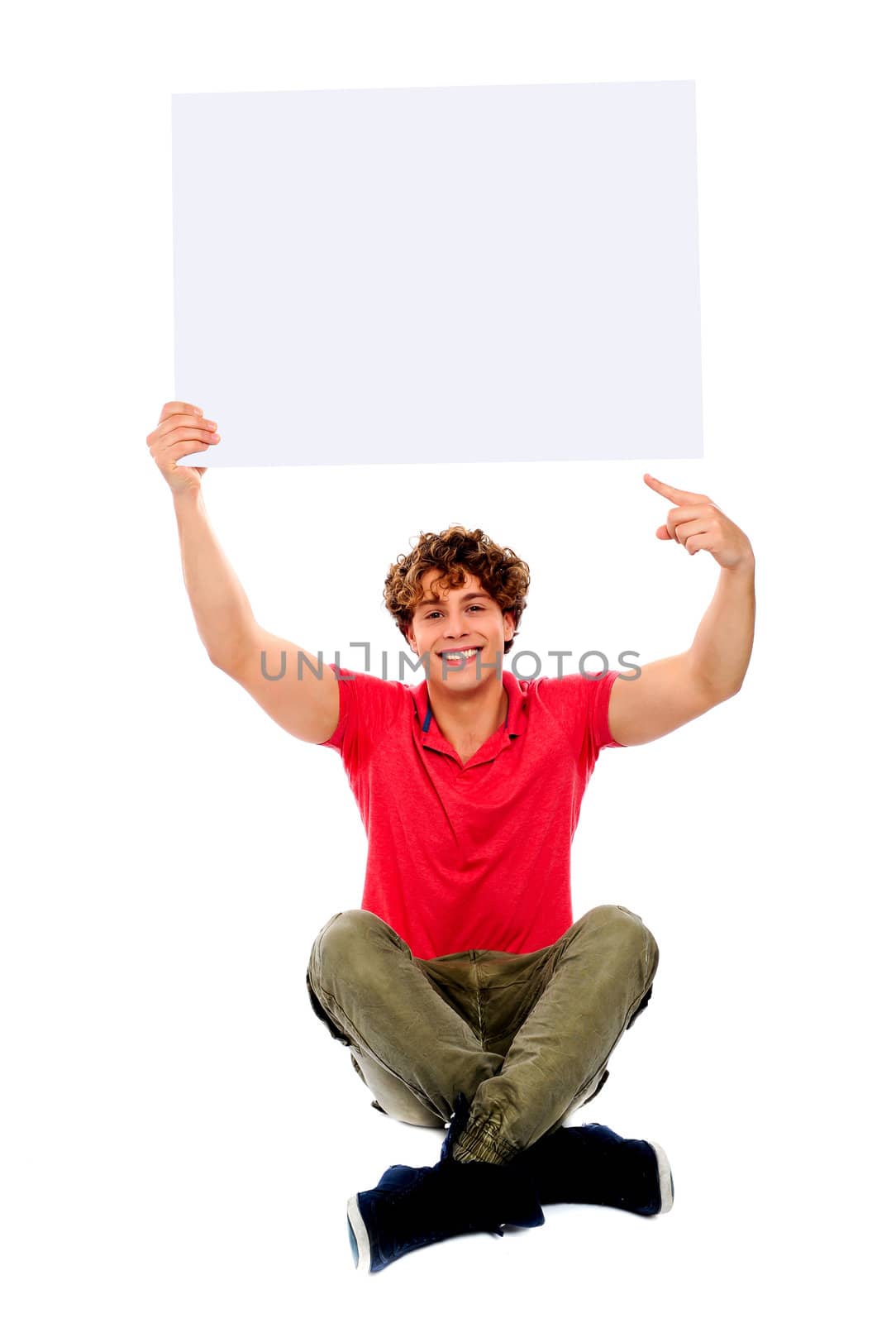 Good looking cool guy pointing towards white blank billboard, seated on floor