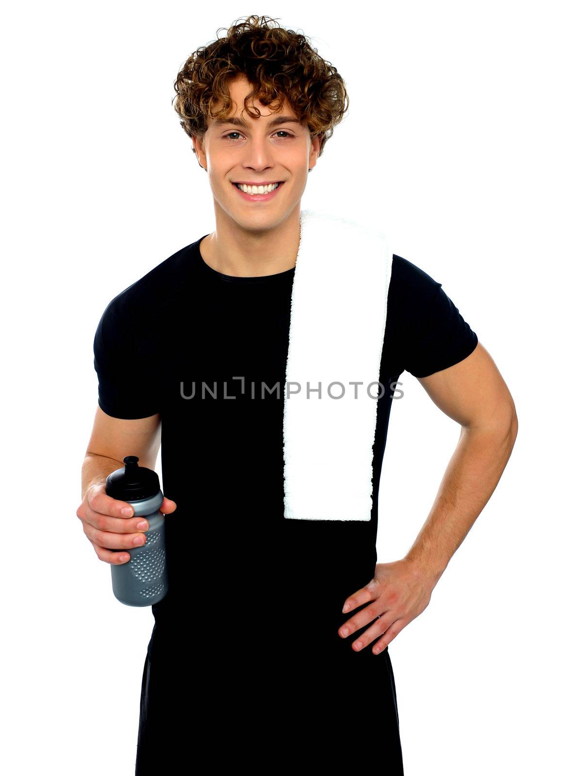Young athletic smiling guy holding sports bottle with towel on shoulders