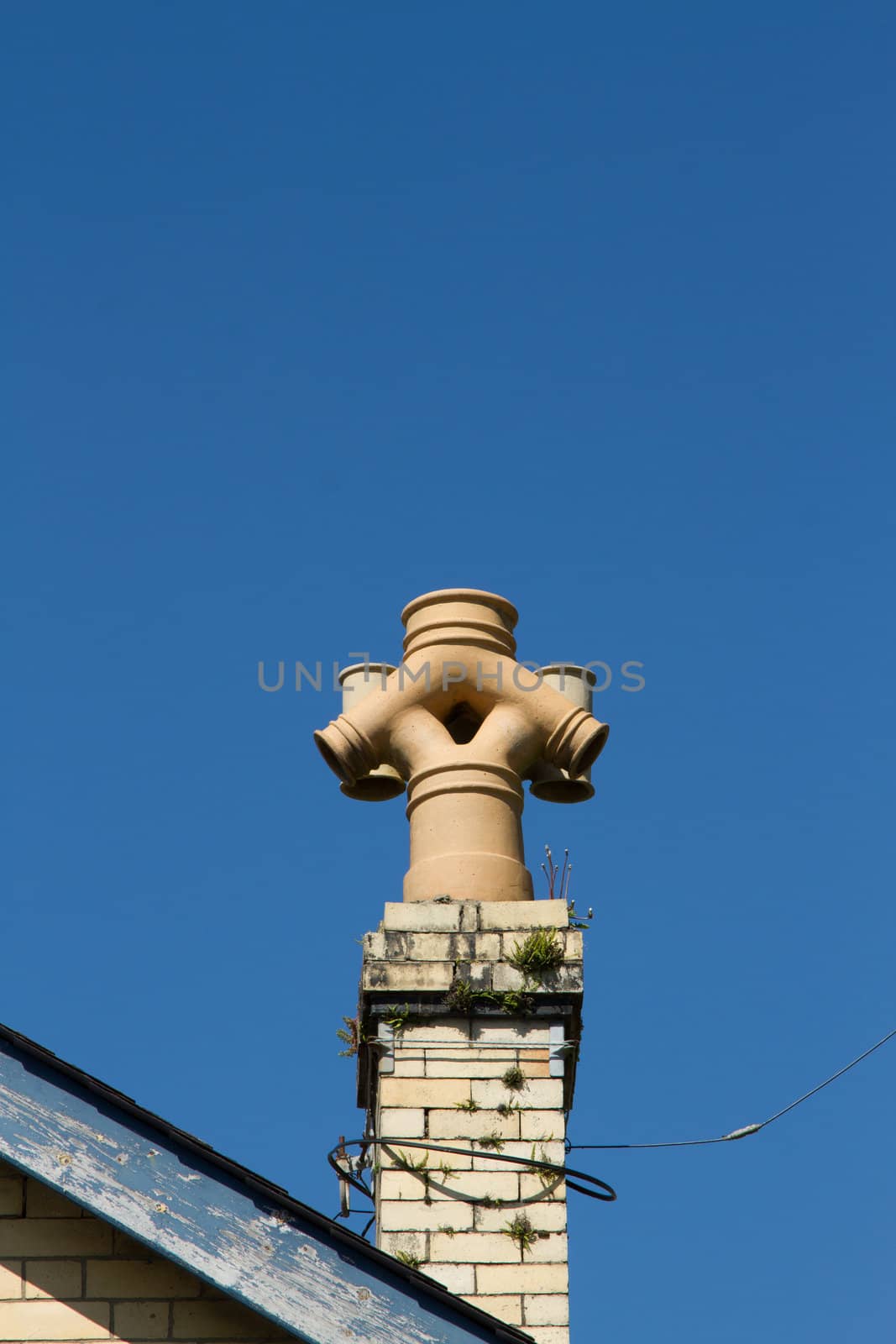 A chimney pot with an unusual design featuring an inverted combination of outlets built on yellow bricks against a blue sky.