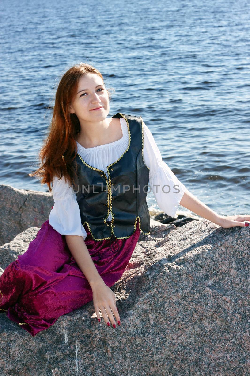 Medieval woman sitting on a big rock near the sea