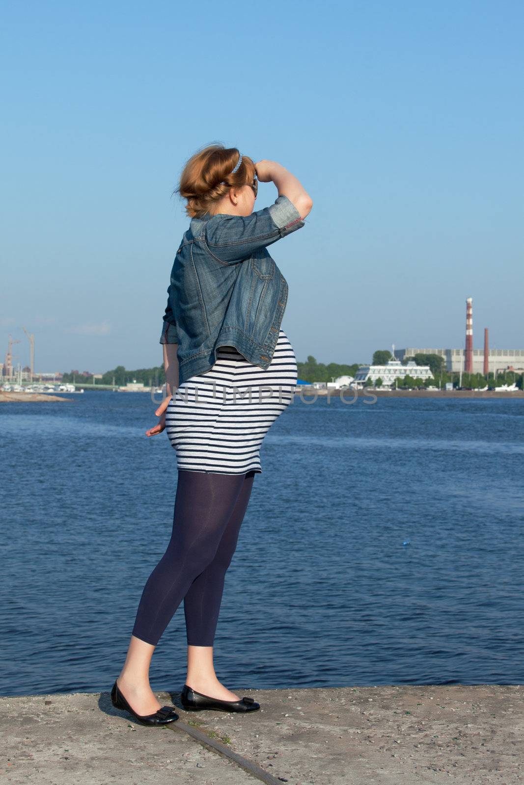 Pregnant woman standing on the pier and looking into the distance