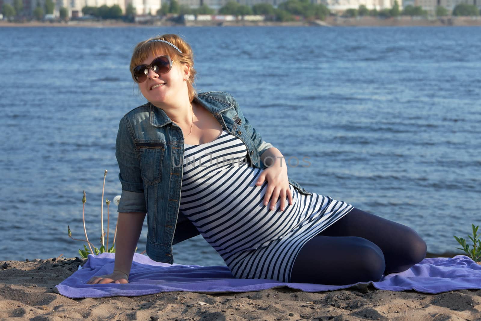 Pregnant woman sitting on the river coast.