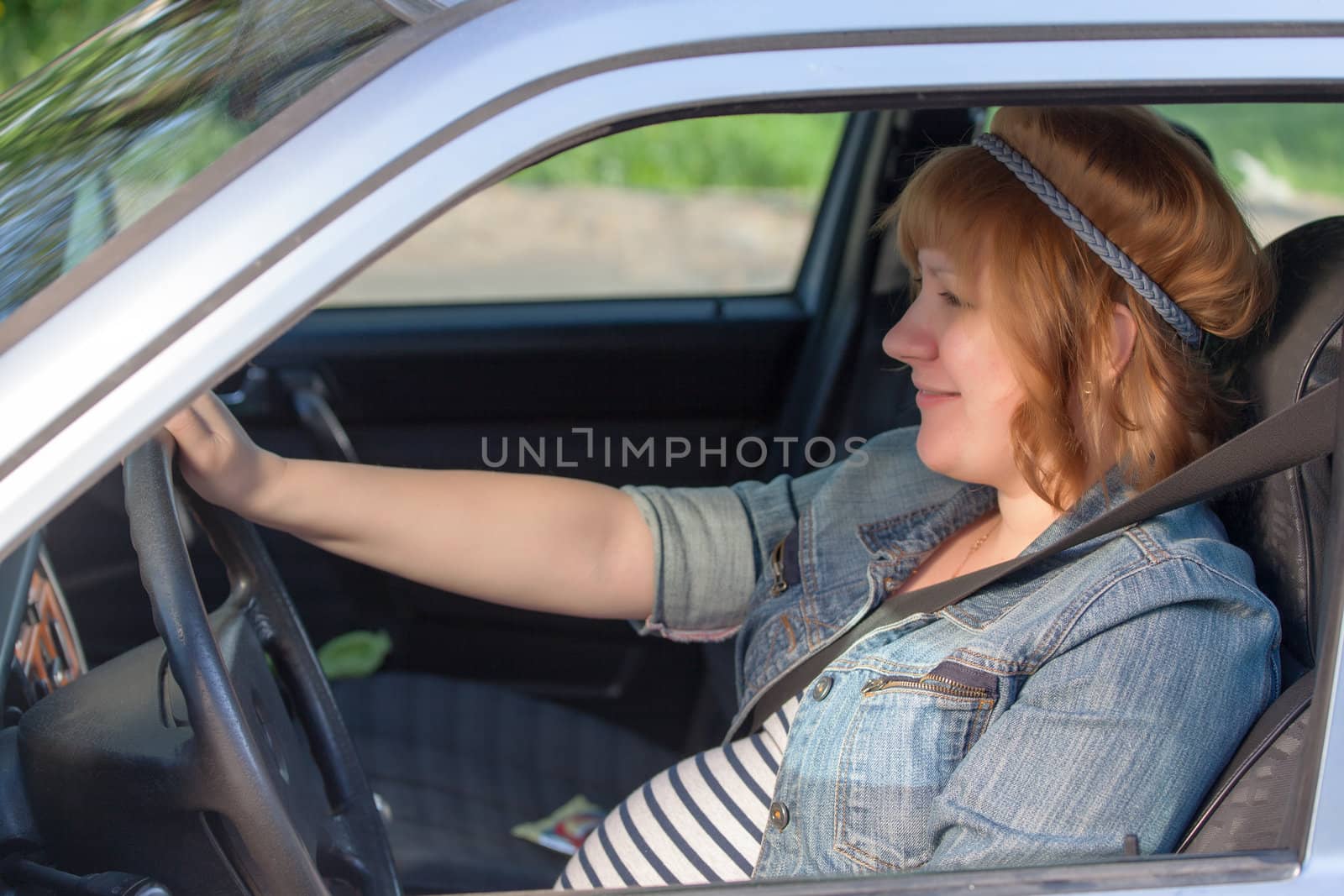 Pregnant woman fastening seat belt in the car by Discovod