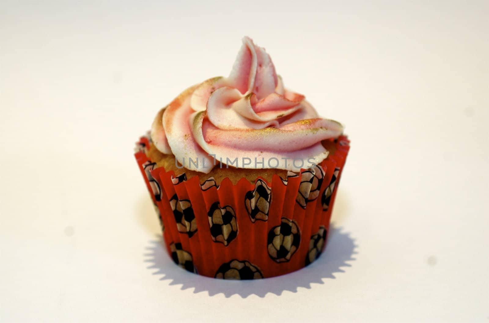 A cupcake with pink frosting on the stop, in a red case decorated with tiny footballs, against a white background with copy space.