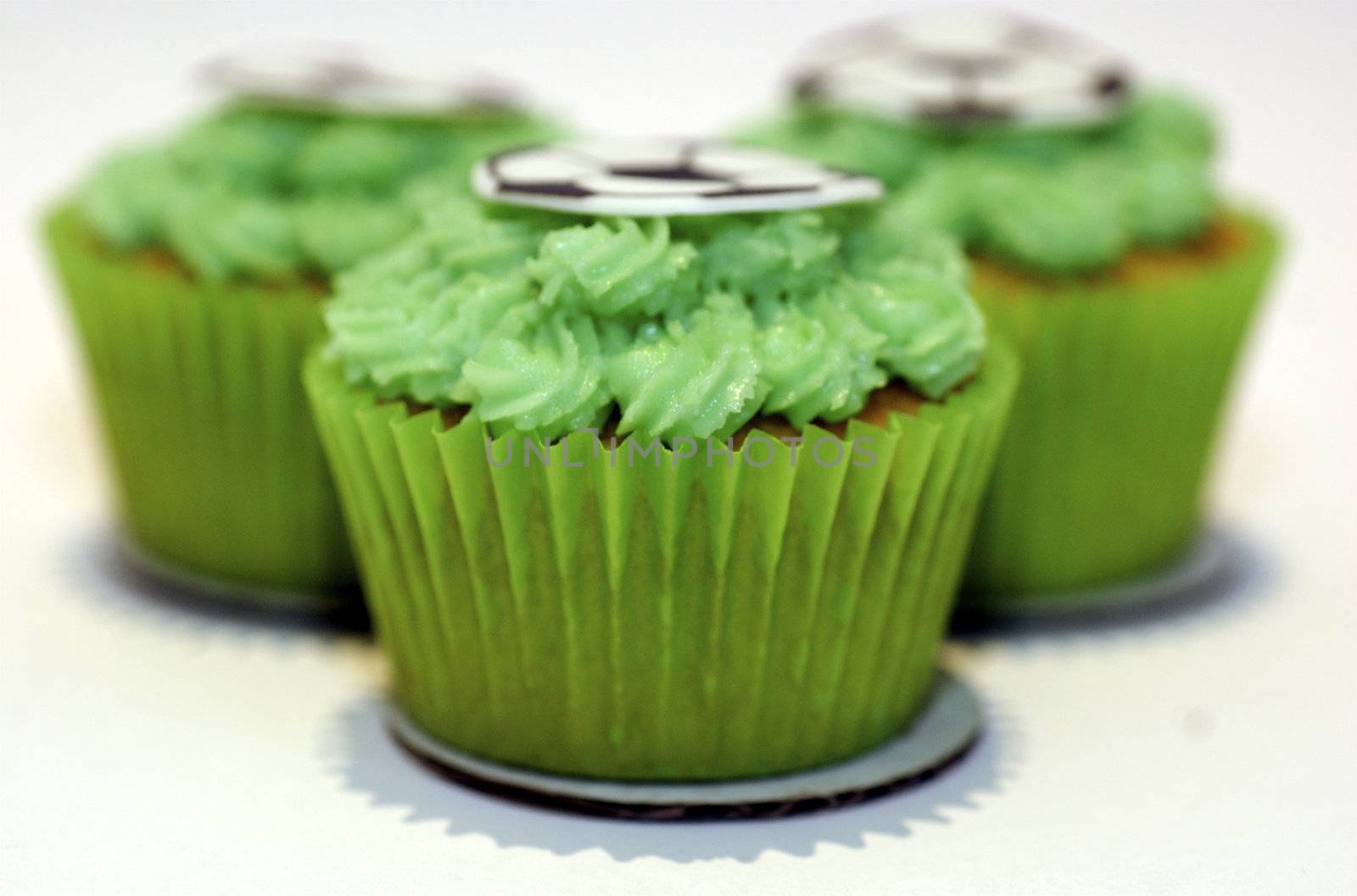 Three cupcakes with green frosting and a flat sugar 'football' on the stop, against a white background with copy space.