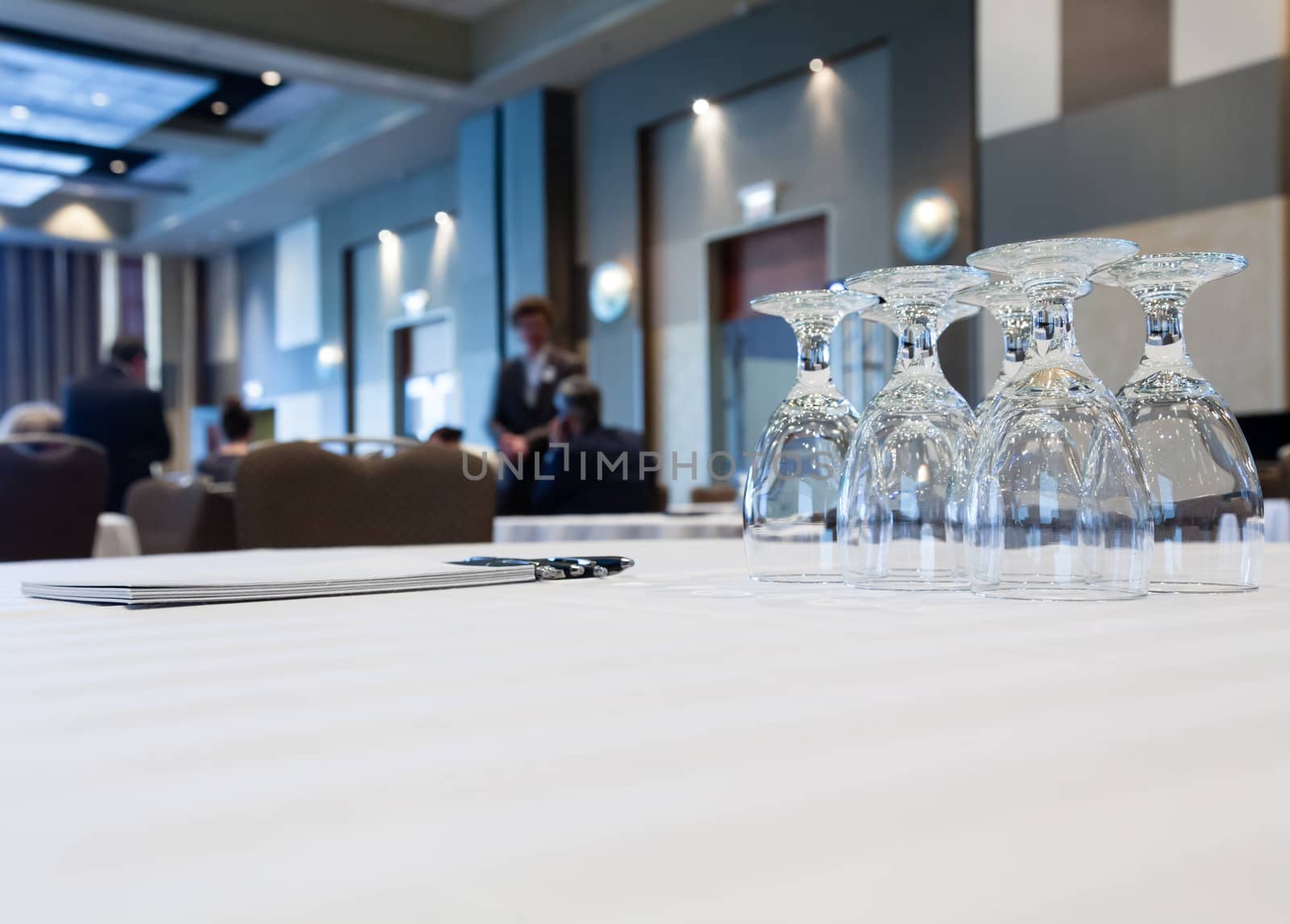 Conference table with glasses and pen paper with people in background