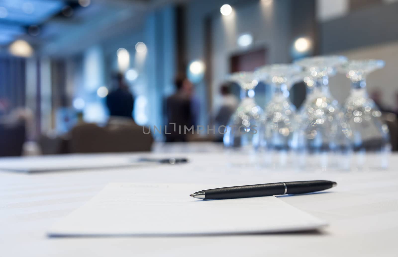 Conference table with glasses and pen paper with people in background