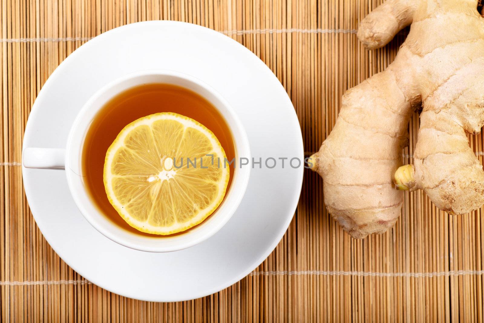 Top view of white cup of green tea with lemon on a white plate and ginger
