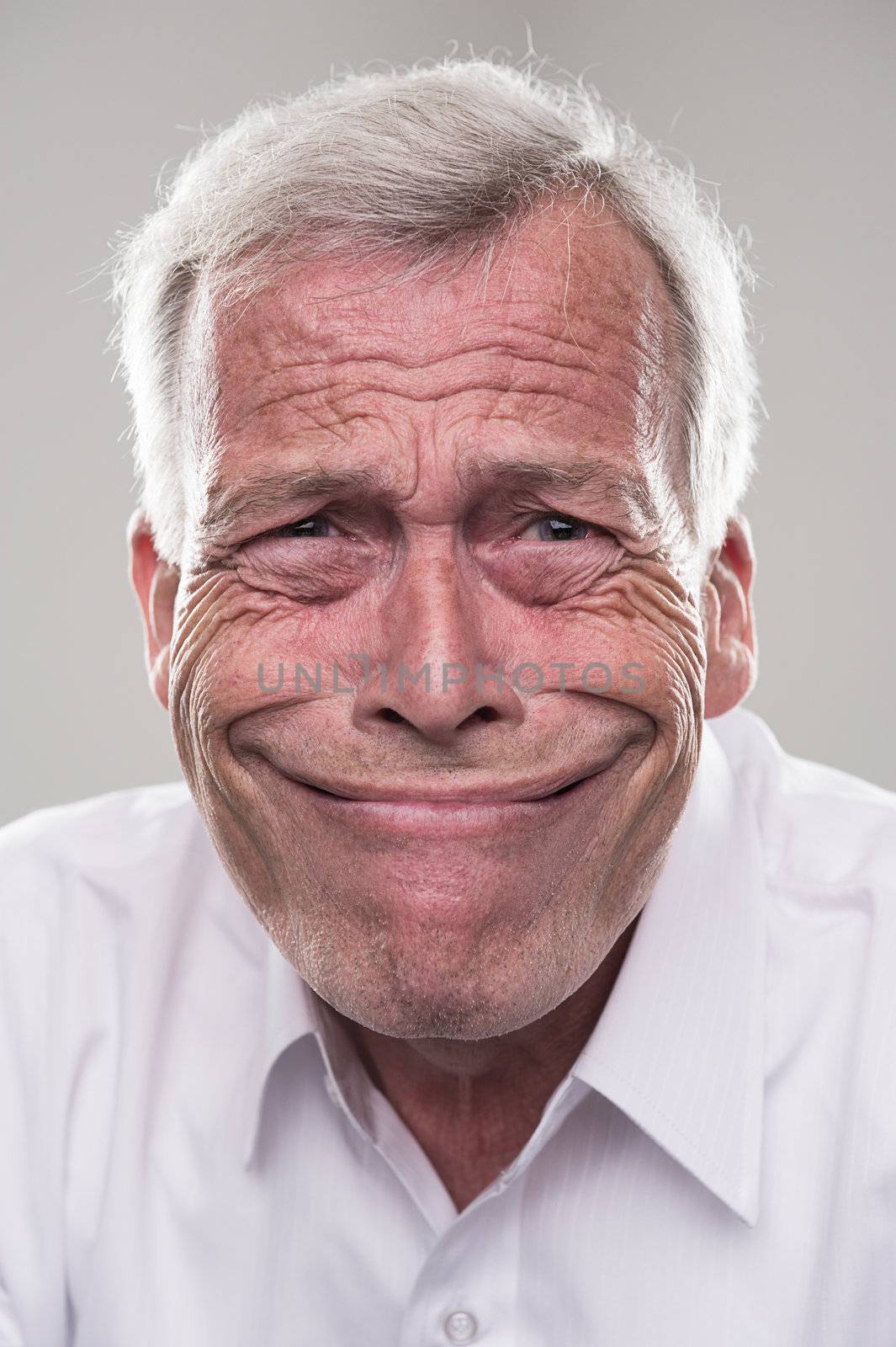 Humorous portrait of a retired gray haired senior man with a wide beaming smile that epitomises the idiom, grinning from ear to ear