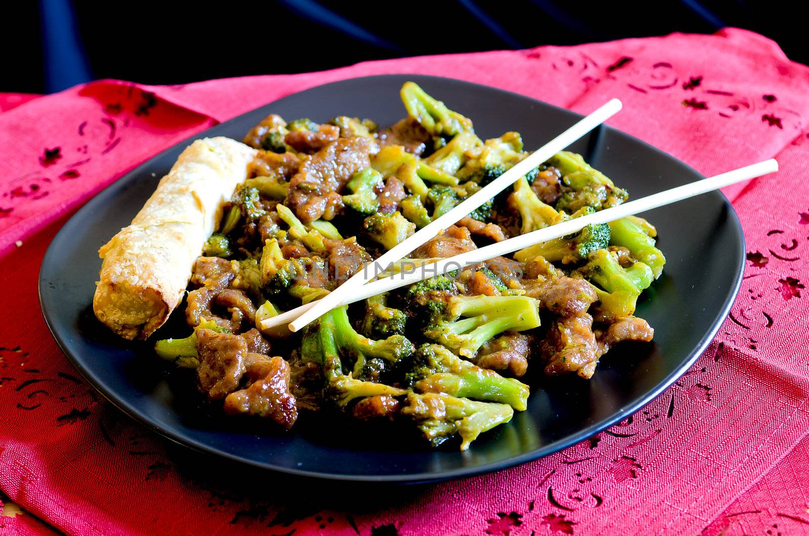 Beef with broccoli with spring roll and chop sticks.