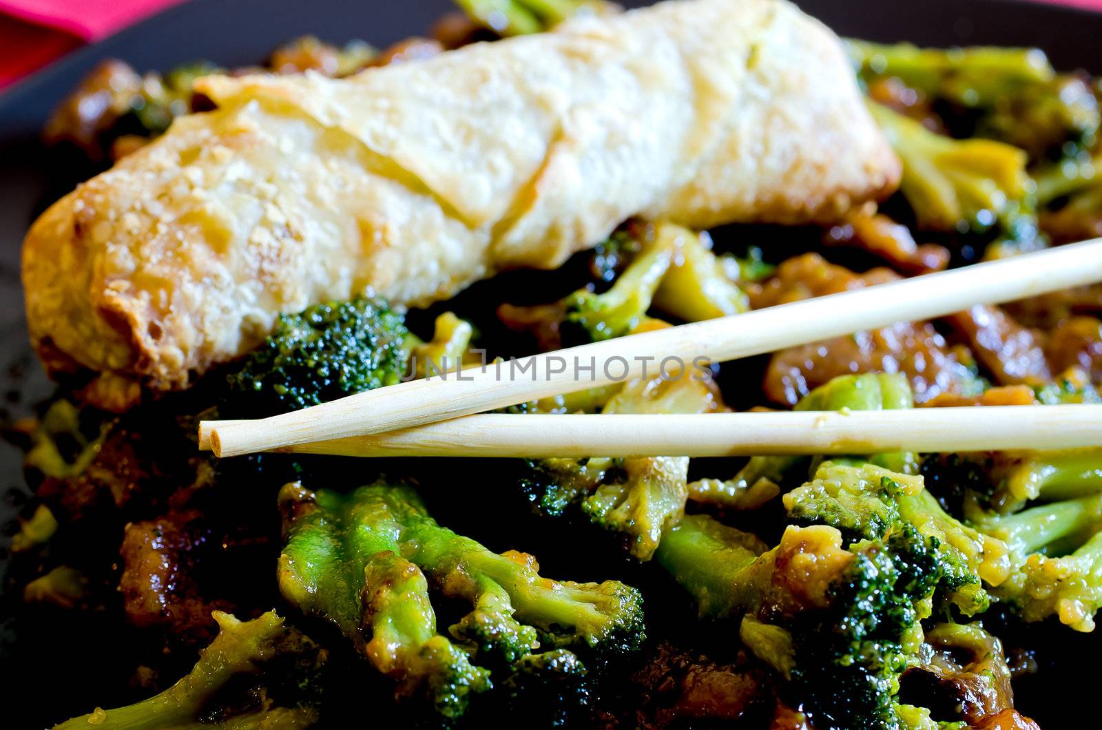 Beef with broccoli with spring roll and chop sticks.
