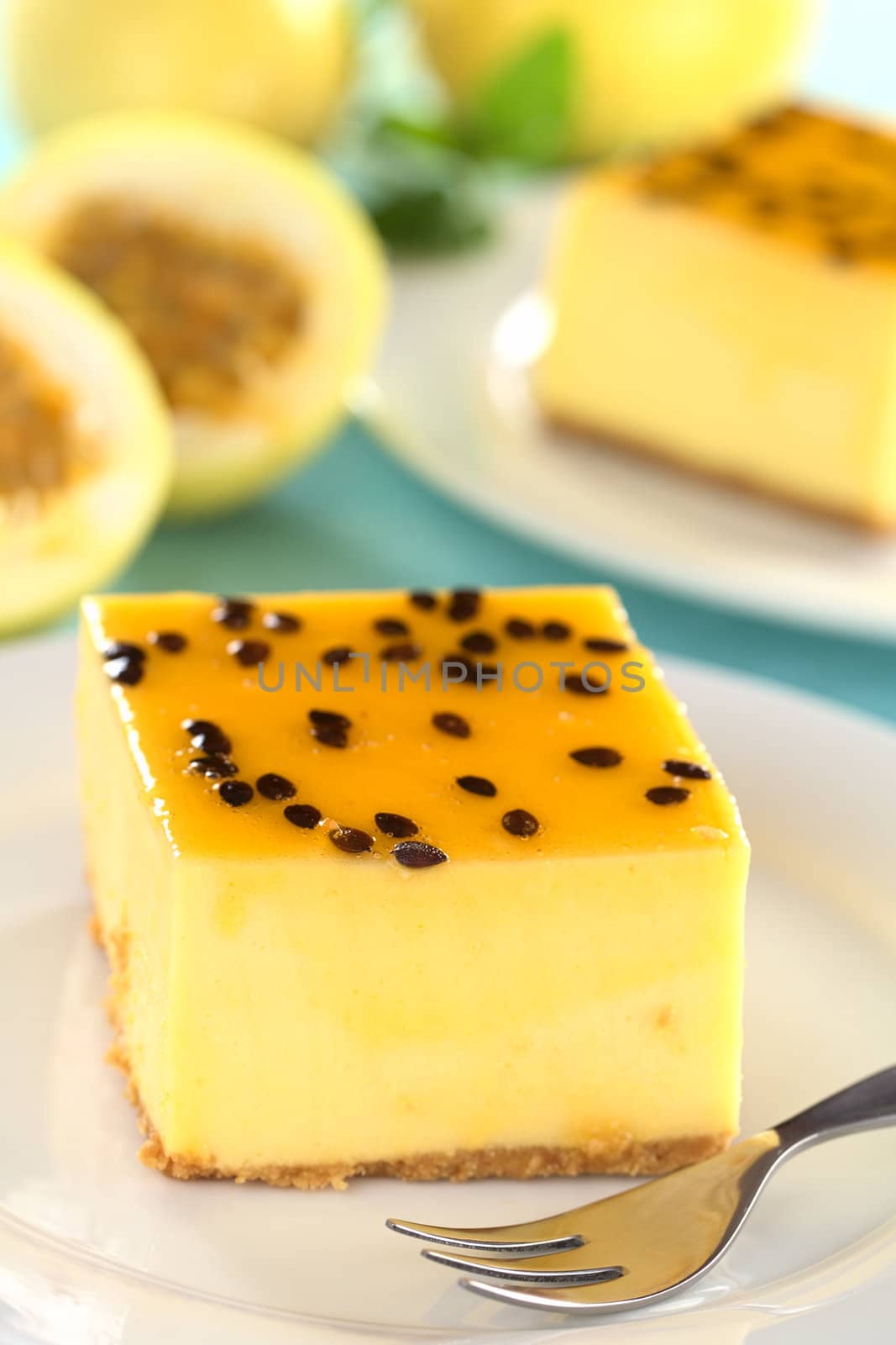 Fresh passion fruit cheesecake dessert on plate with pastry fork with another cake and yellow passion fruits in the back (Selective Focus, Focus on the left upper front edge of the cake)