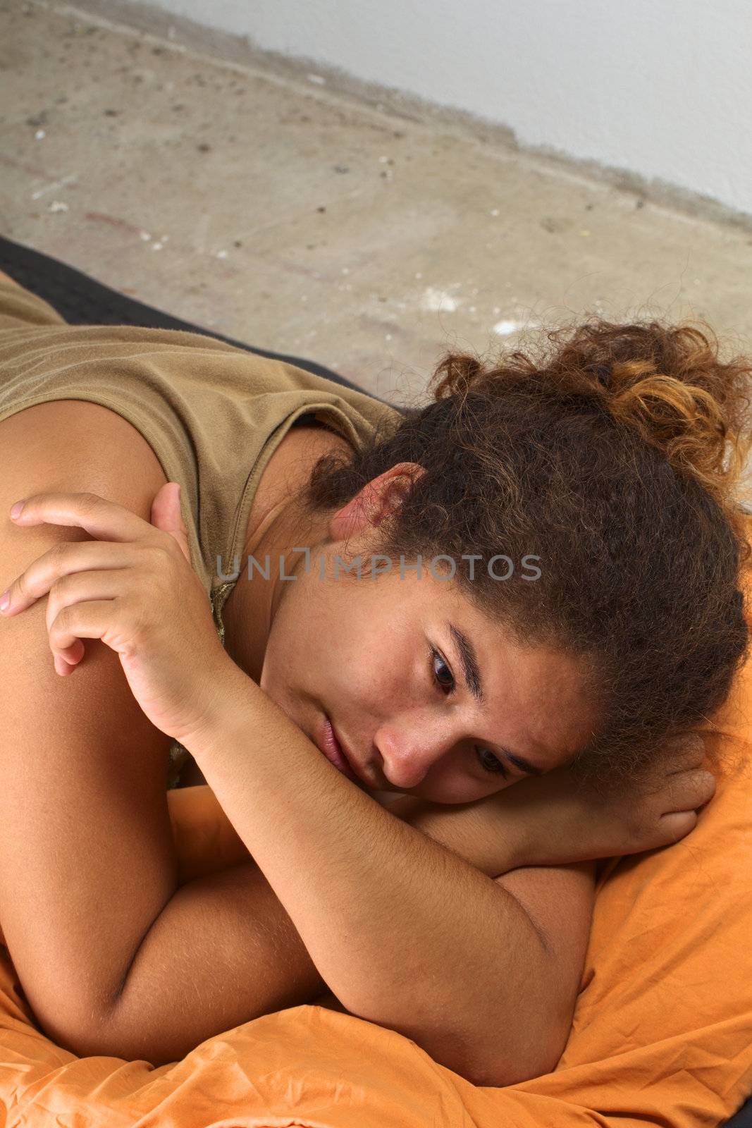 Young Peruvian woman squatting an abandoned house, lying on the floor on a mat and sleeping bag looking sadly (Selective Focus, Focus on the right eye)