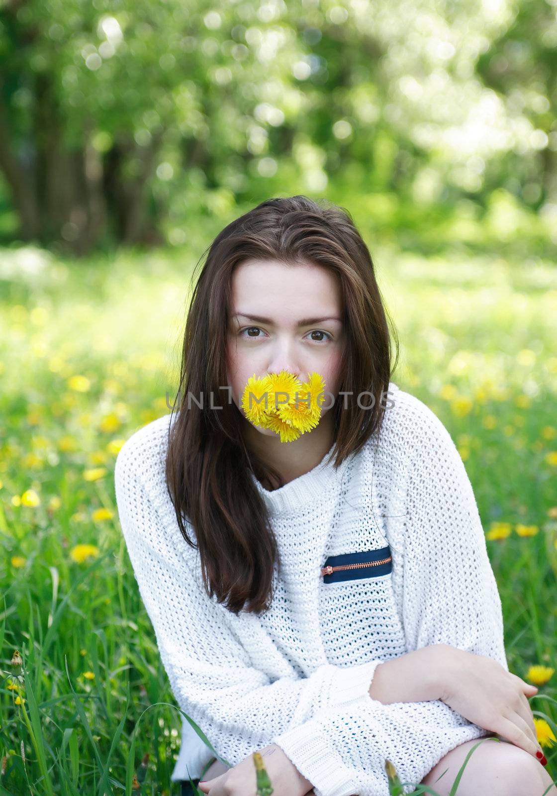 Beauty teenage girl with yellow dandelions in her mouth on green summer background