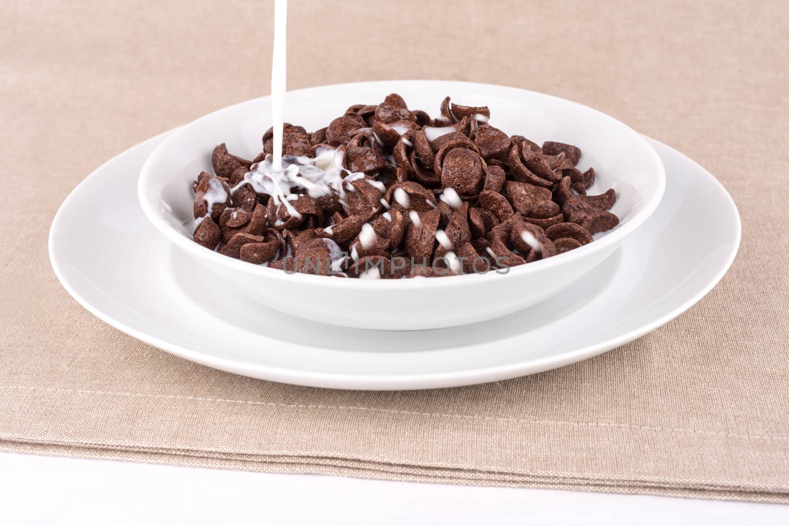 Milk pouring into a dish with chocolate cereal flakes.