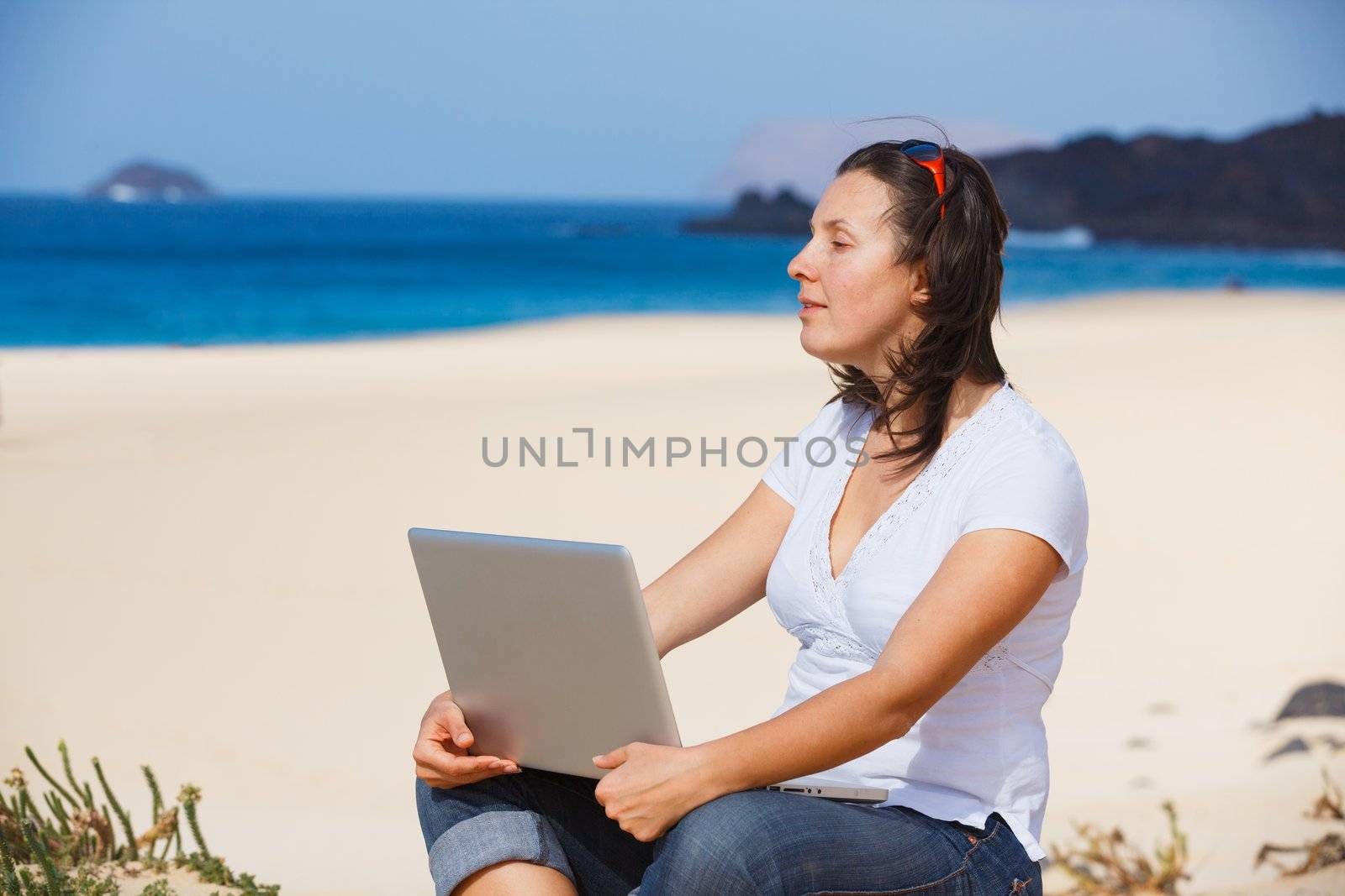 Young woman sitting on the exotic tropical beach with laptop computer
