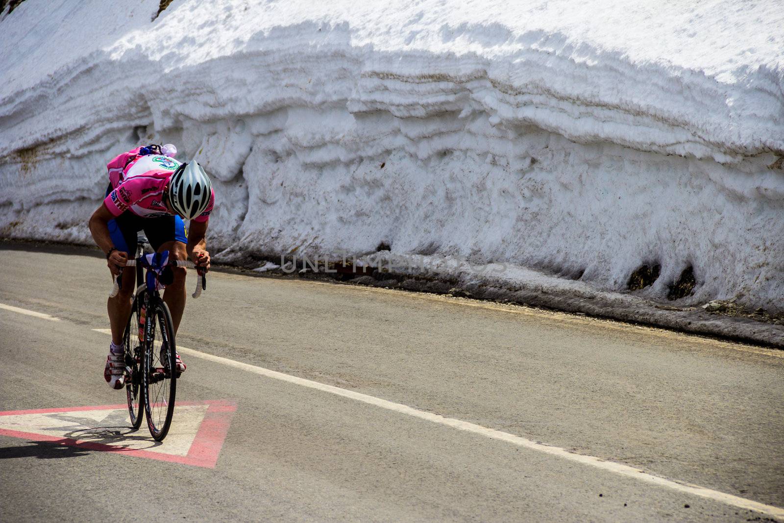 Cyclist cycling up a road next to a wall of snow