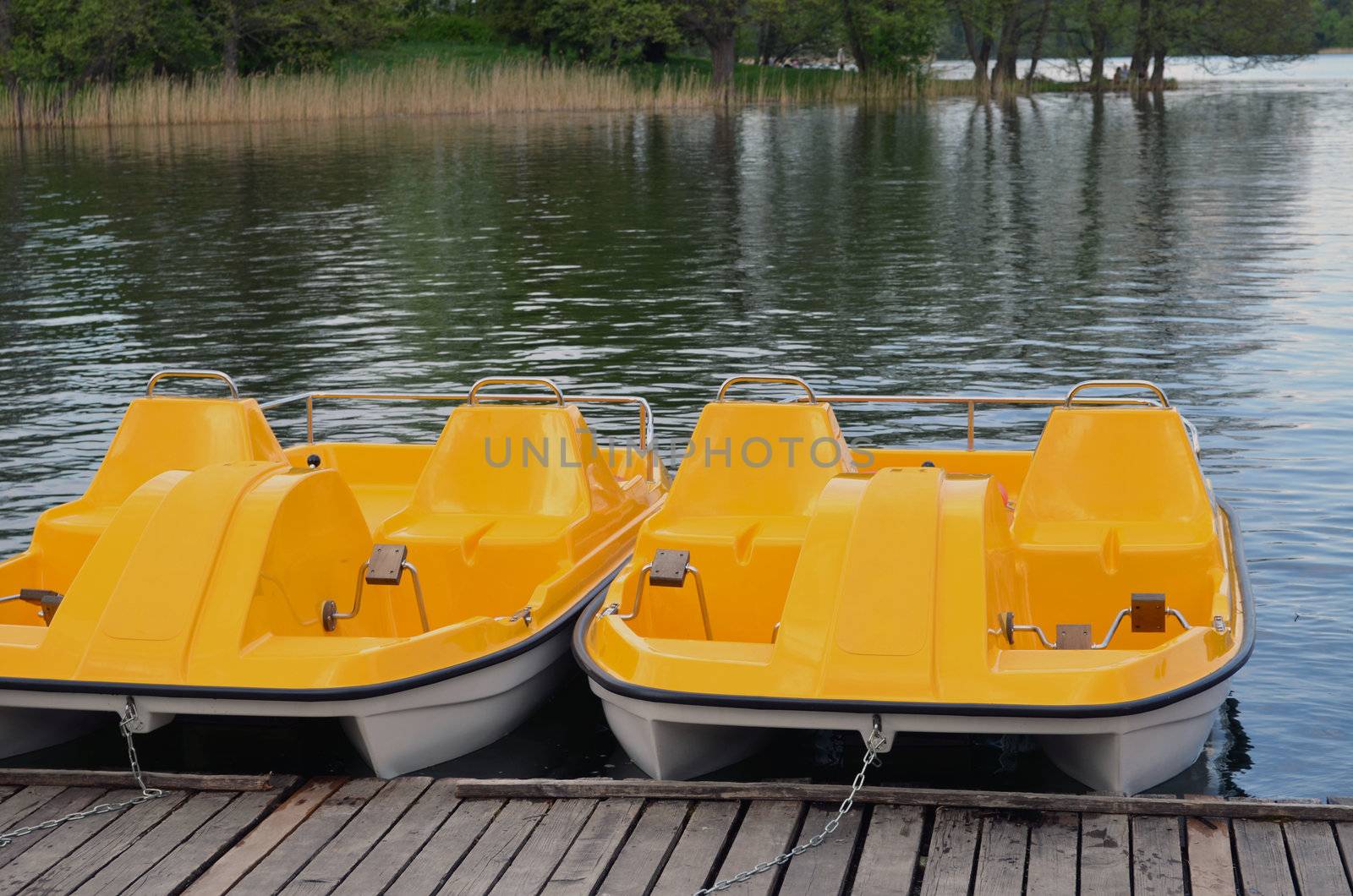 Yellow water bicycles locked at lake marina. Active recreation objects.