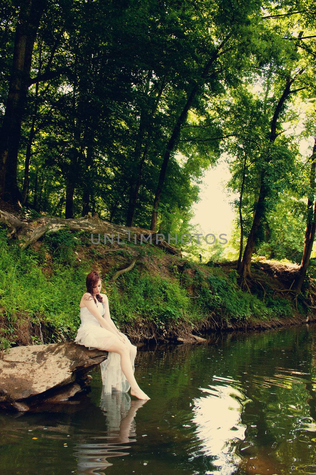 A bride sitting on a rock on a riverbank