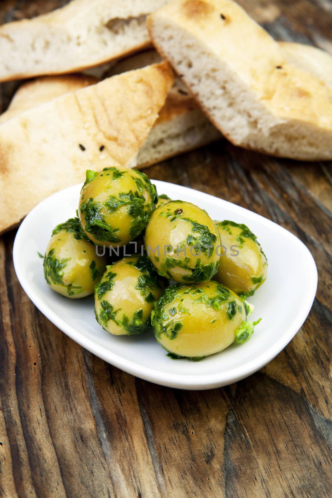 green olives with fresh bread and herbs on wooden background