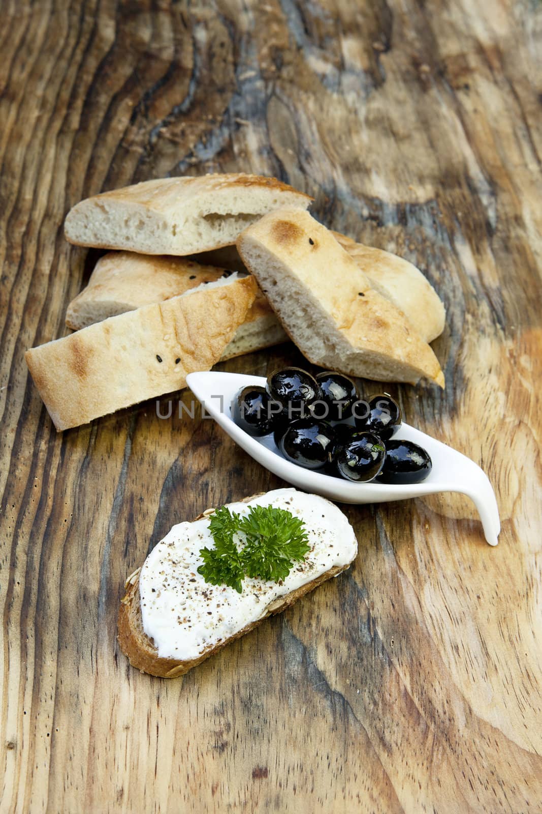 green olives with fresh bread and herbs on wooden background