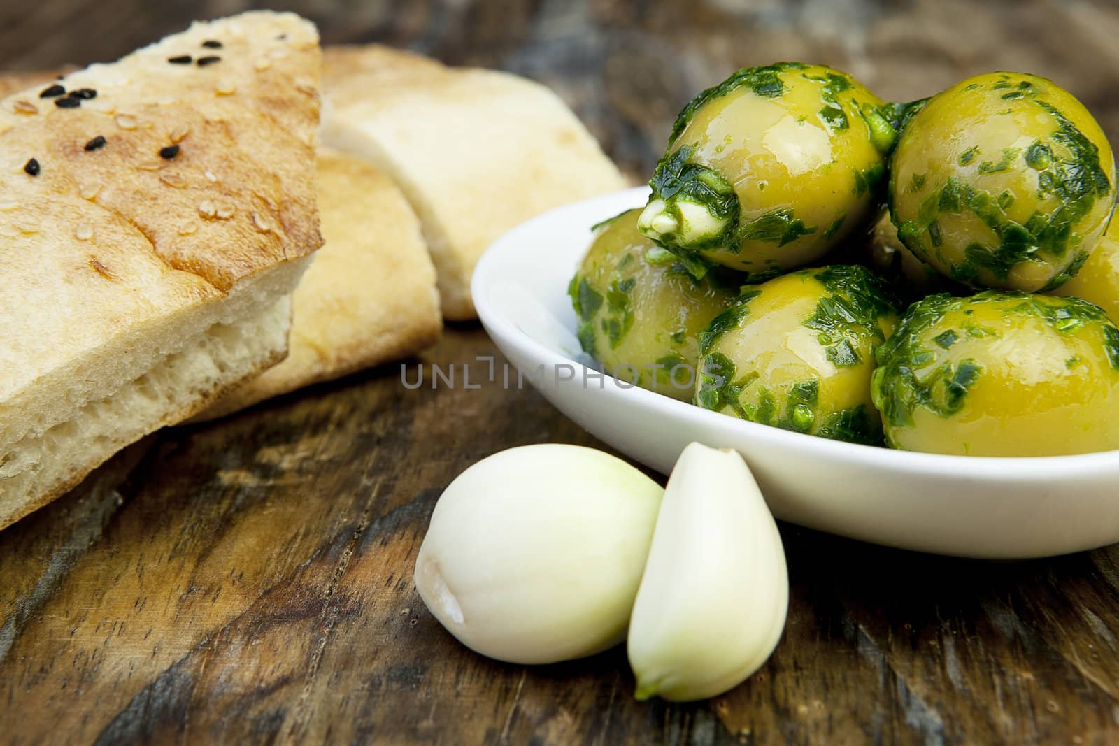 green olives with fresh bread and herbs on wooden background