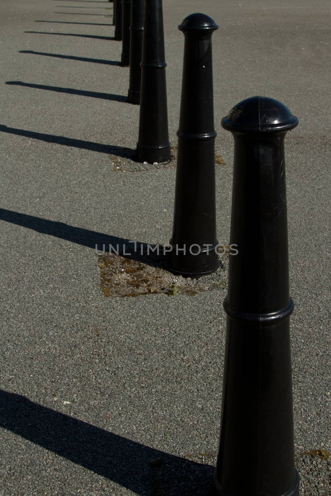 A set of black painted metal posts spaced out as a traffic barrier set in tarmac.