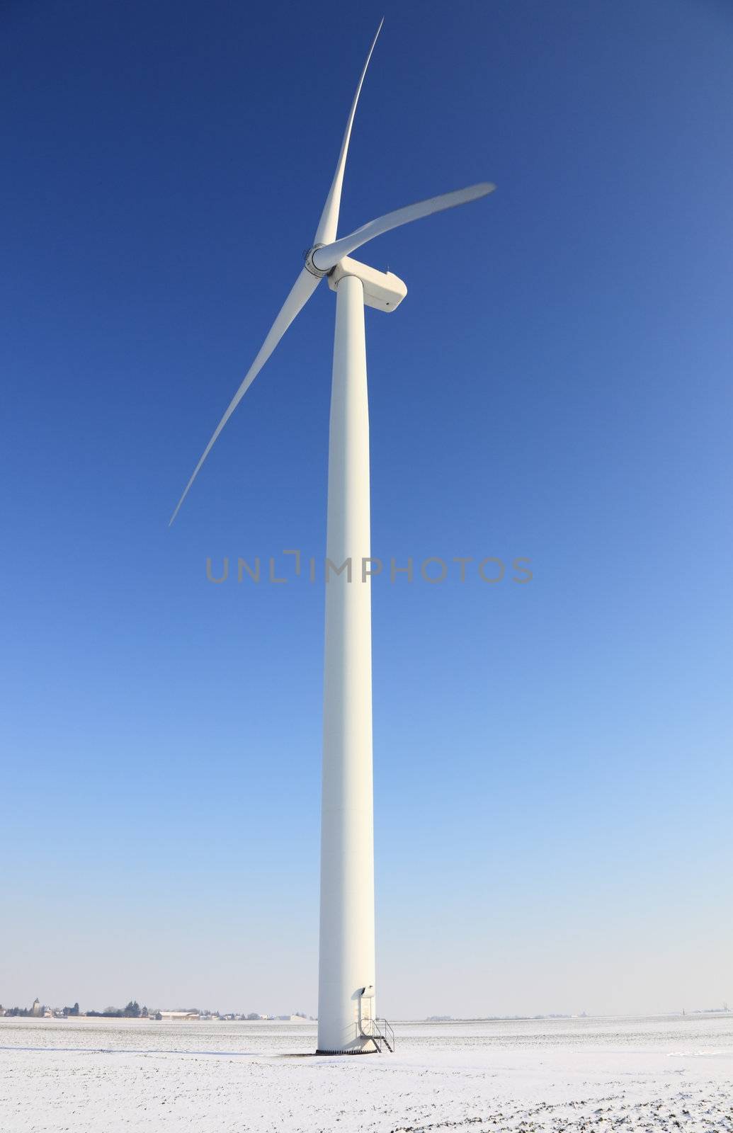 Wind turbine in a field covered by sbow in winter.There is a little motion blur at the tips of the blades.