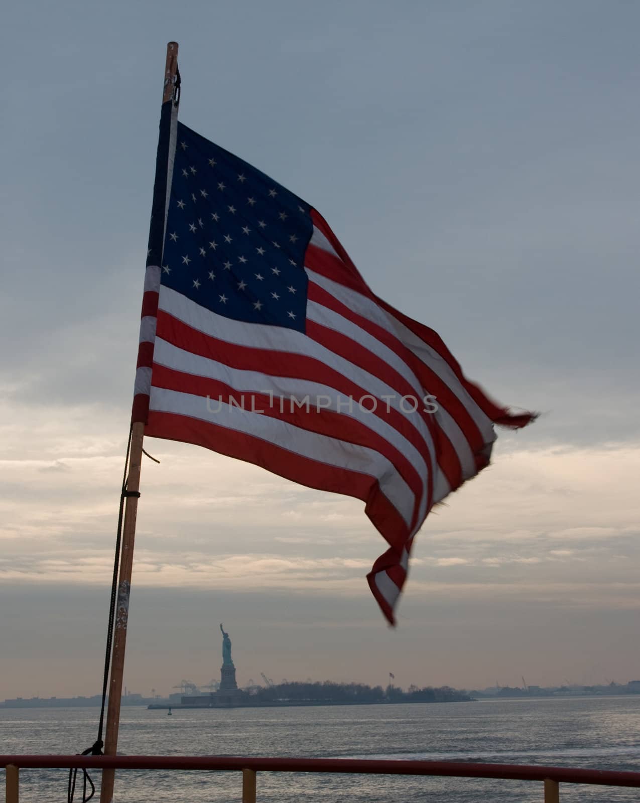 The United States flag wrapped around the Statue of Liberty in the distance, as seen from the Ferry.