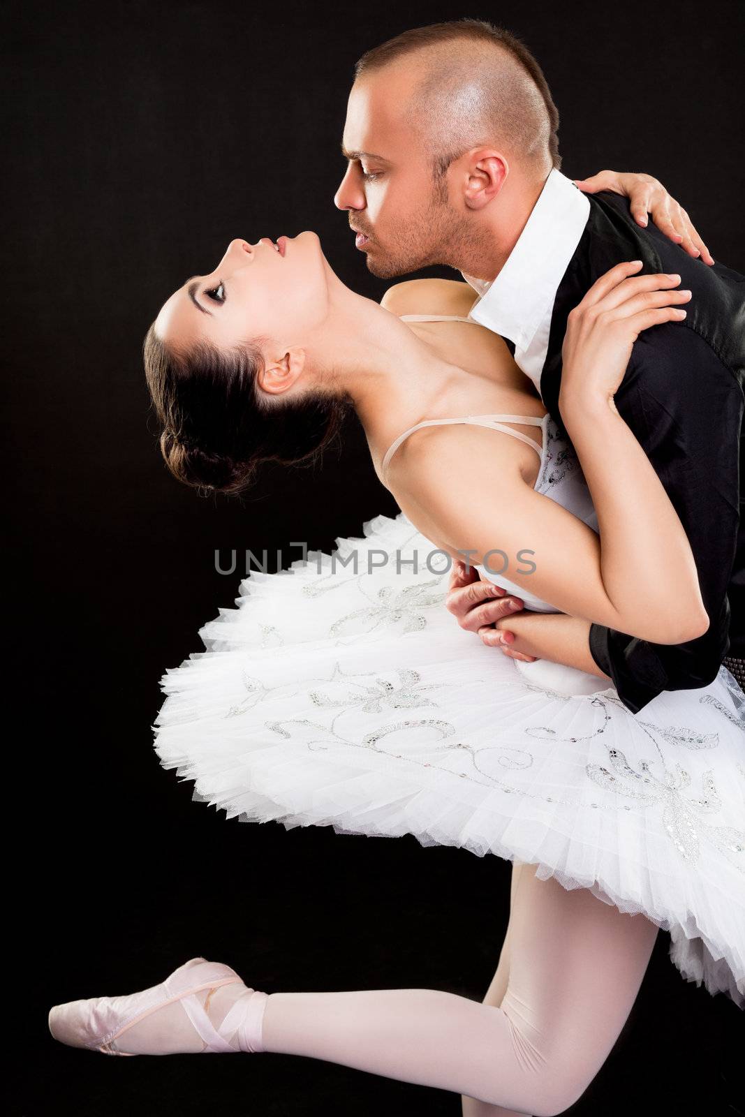 Man passionately hugging beautiful ballerina on dark background