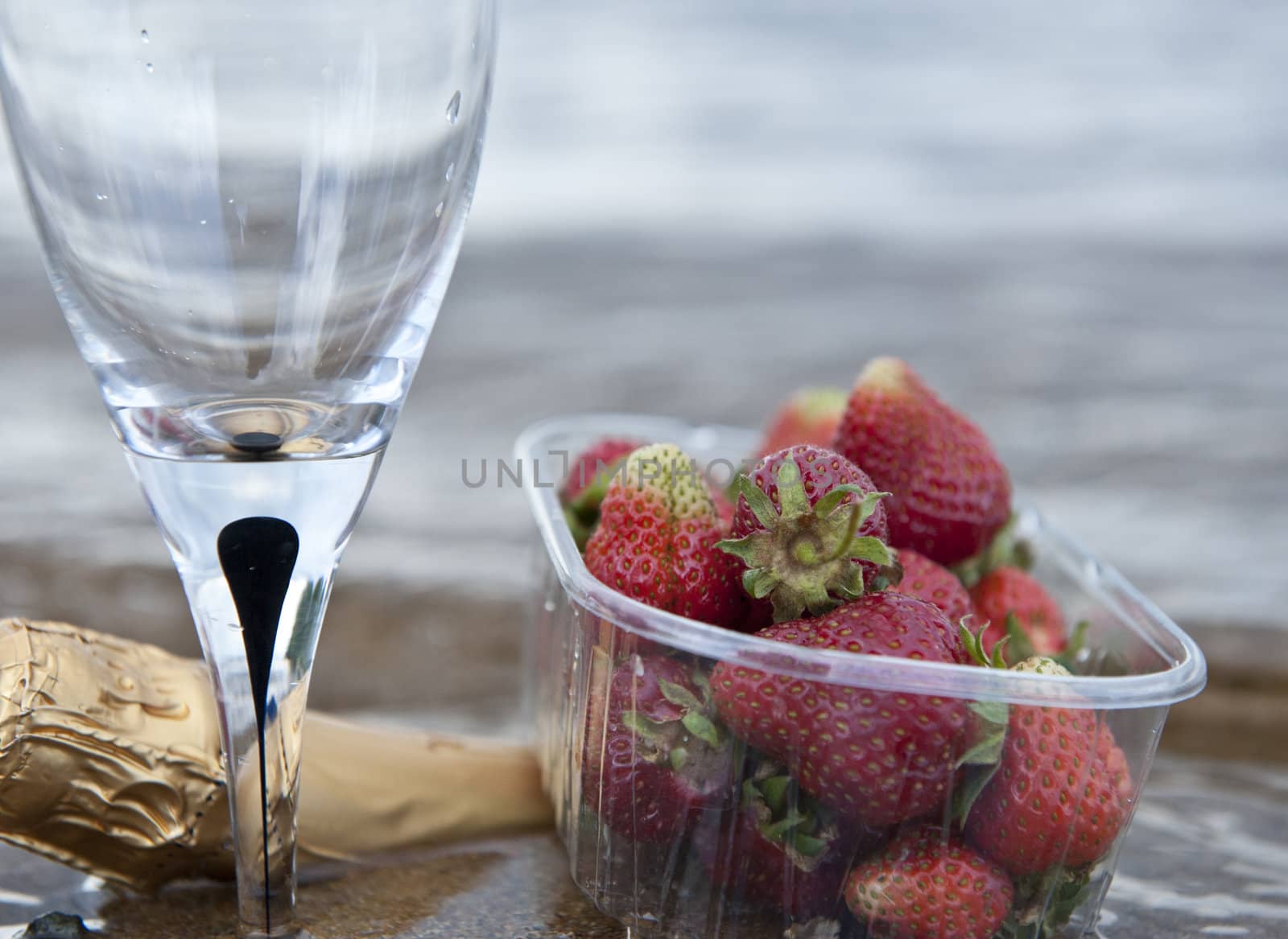 Cloesup of some strawberries a glass and a bottle of wine by the seaside