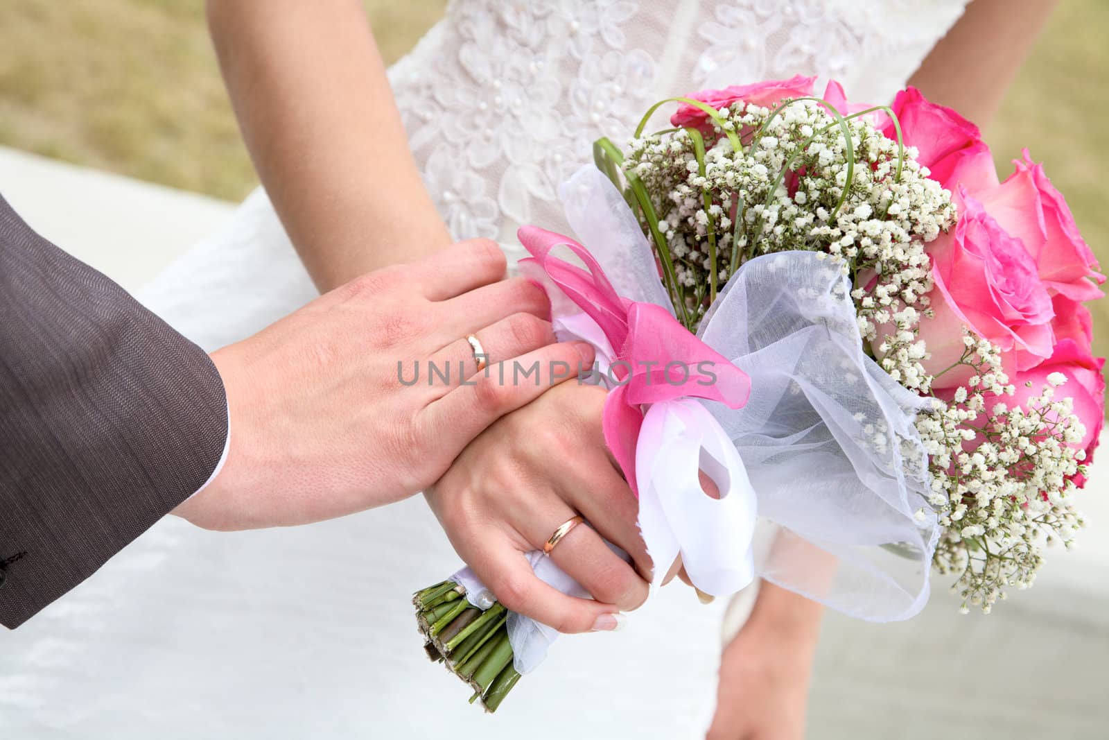 Hands and rings with wedding bouquet against a grass