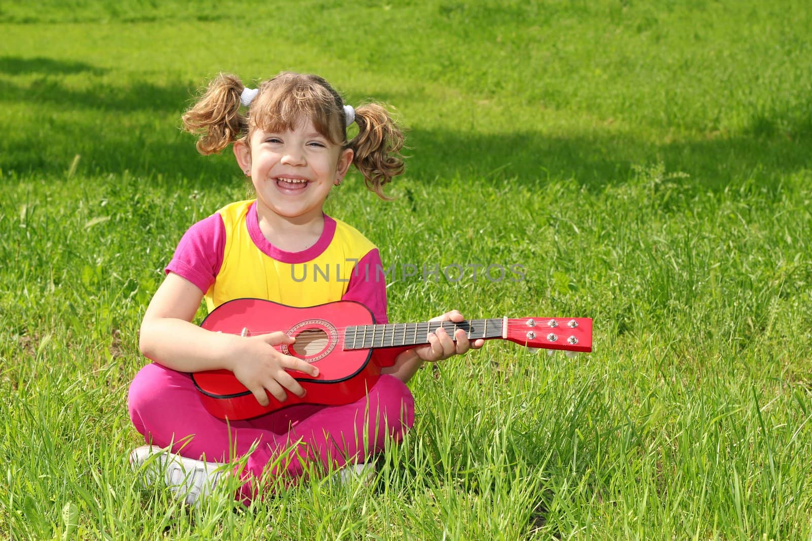 little girl sitting on grass and play guitar