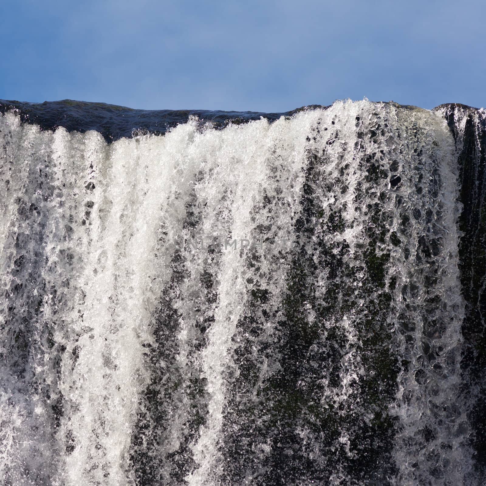 Water cascading over rock edge forming a waterfall by PiLens
